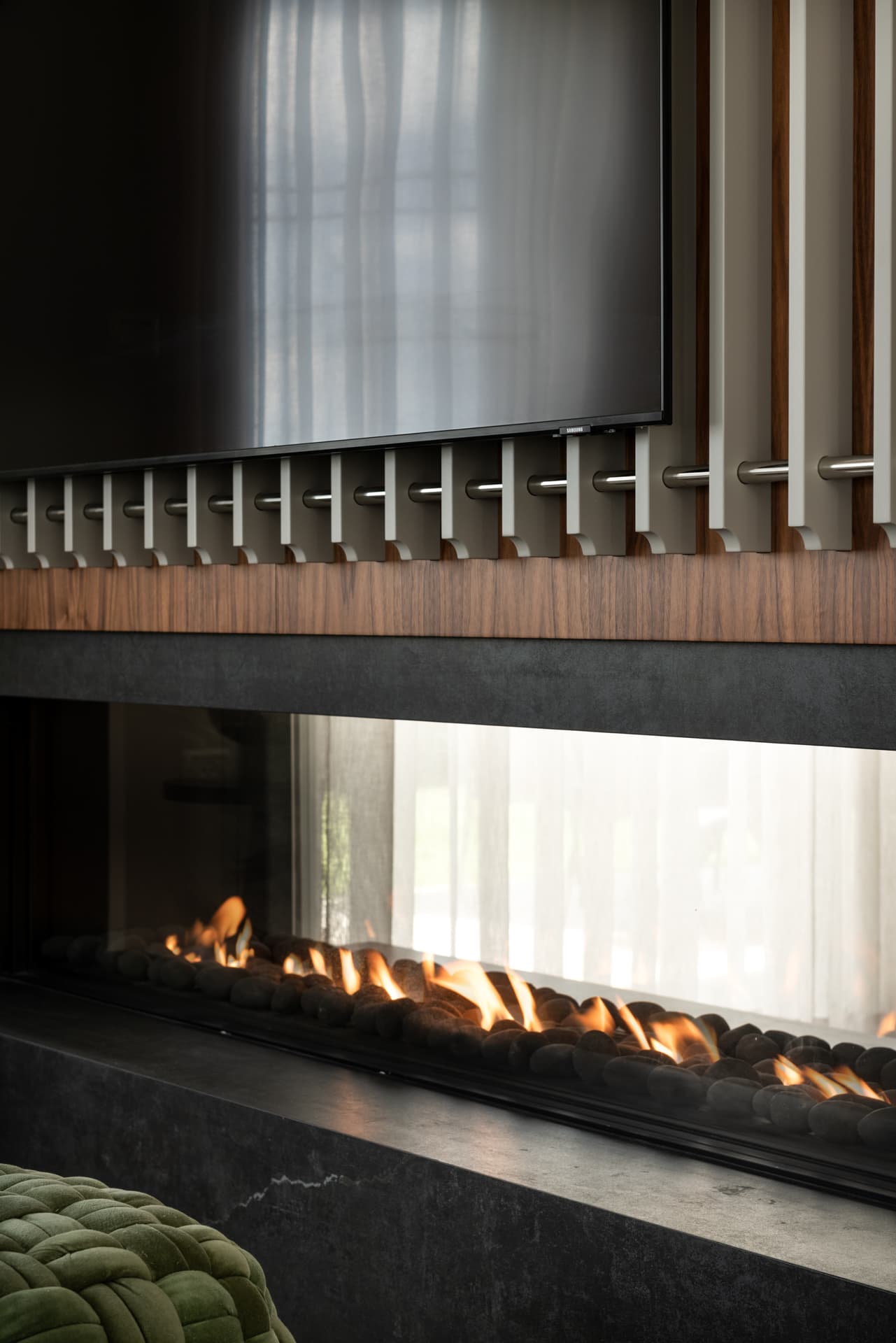 Linear gas fire behind glass on a dark stone base, beneath slatted walnut panelling and a screen in the living room of Pistachio