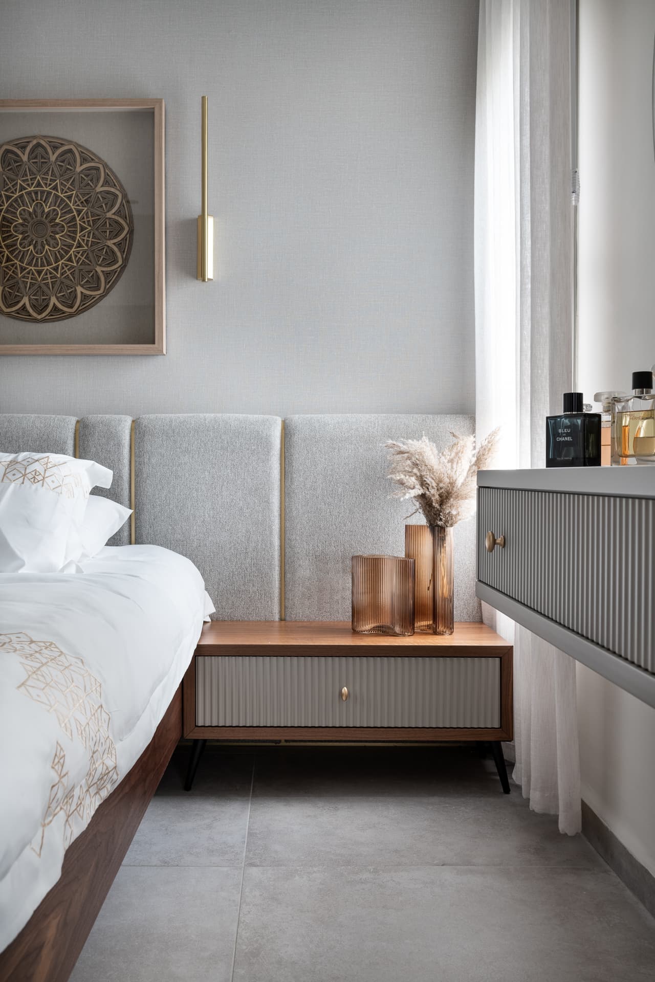 Walnut nightstand with fluted grey drawer and amber ribbed glass vases beside a grey panelled headboard in the master bedroom of Pistachio