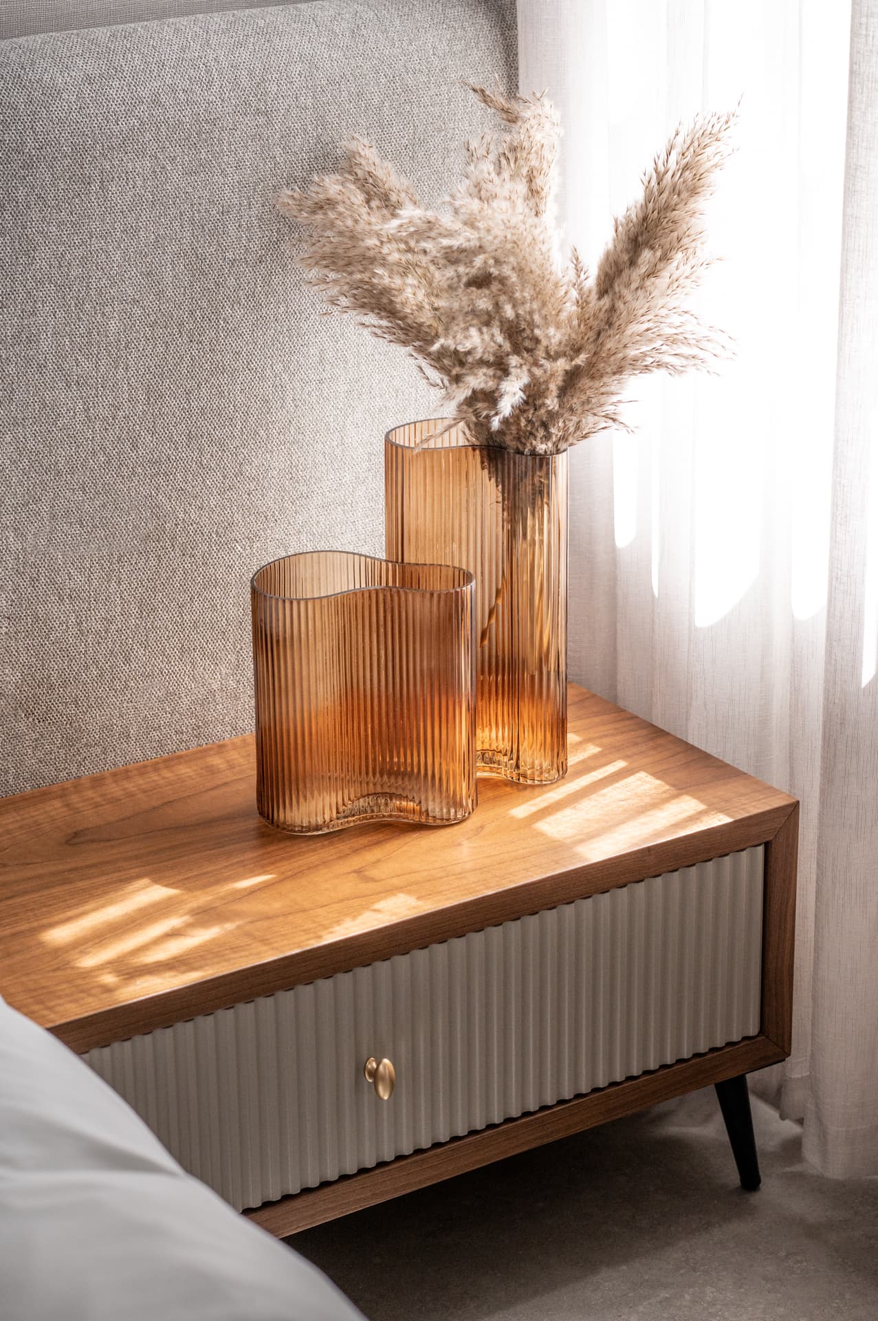 Amber ribbed glass vases with dried pampas grass on a walnut nightstand in soft window light in the master bedroom of Pistachio