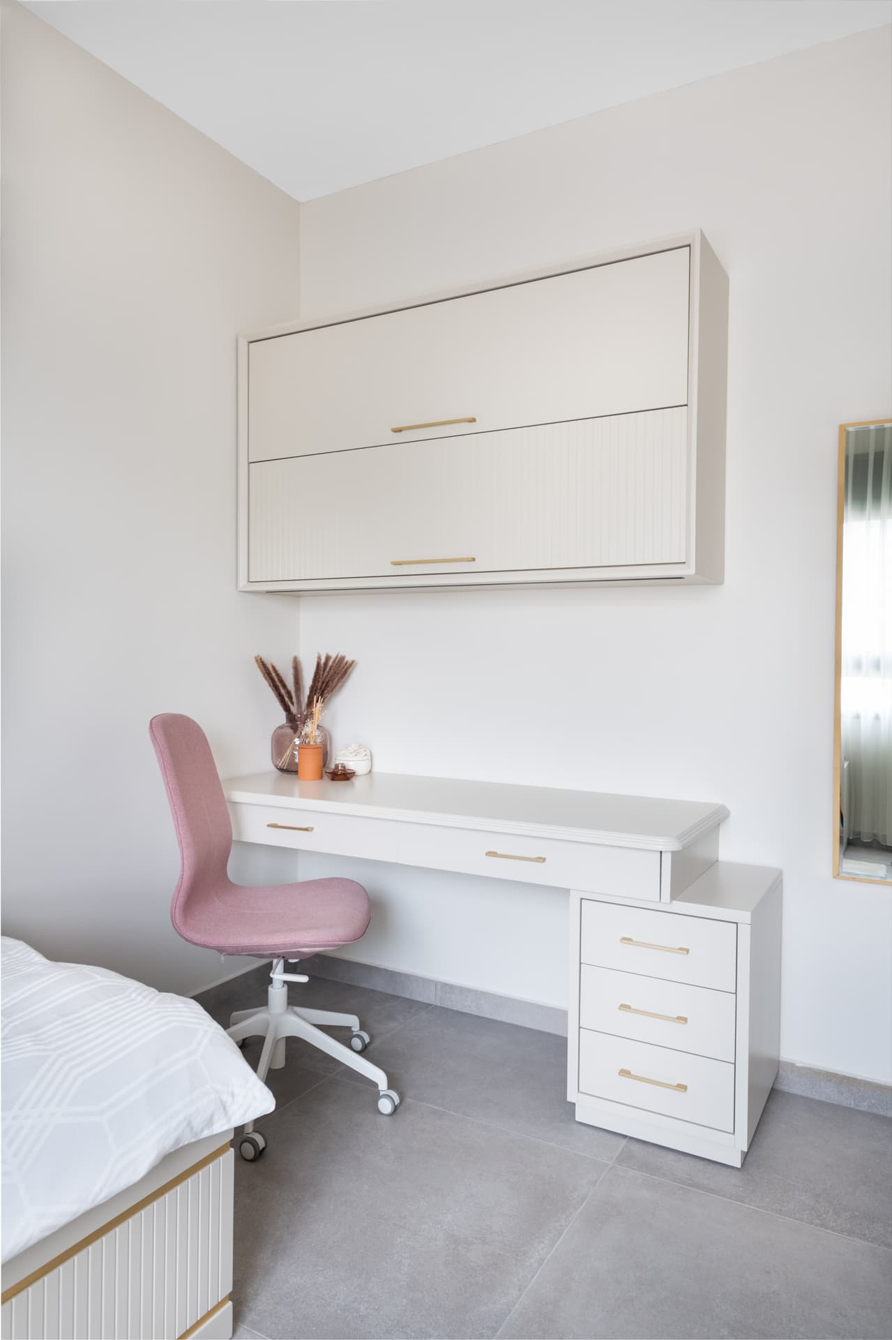 Cream study desk with brass pulls, a wall-hung cabinet above and a blush swivel chair in the corner of the girls bedroom of Pistachio