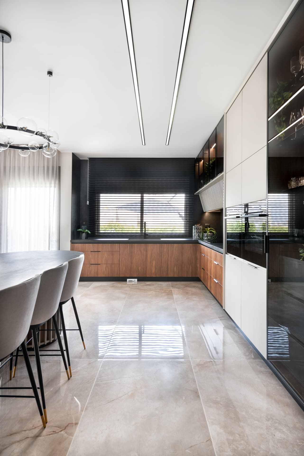 Walnut base cabinets under a dark window wall, with a tall smoked-glass display wall and linear ceiling lights in the kitchen of Pistachio