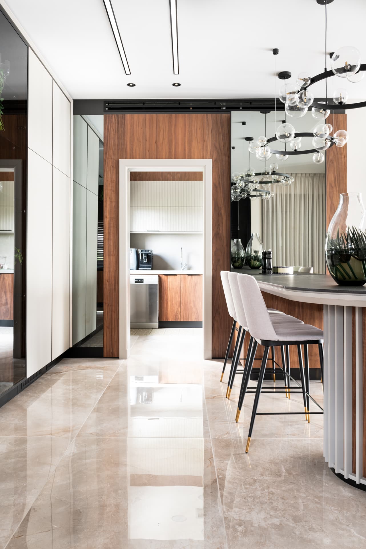 Slatted island base with pale stools beside a walnut-clad doorway into a small kitchen, with tall cream and mirror cabinets in Pistachio