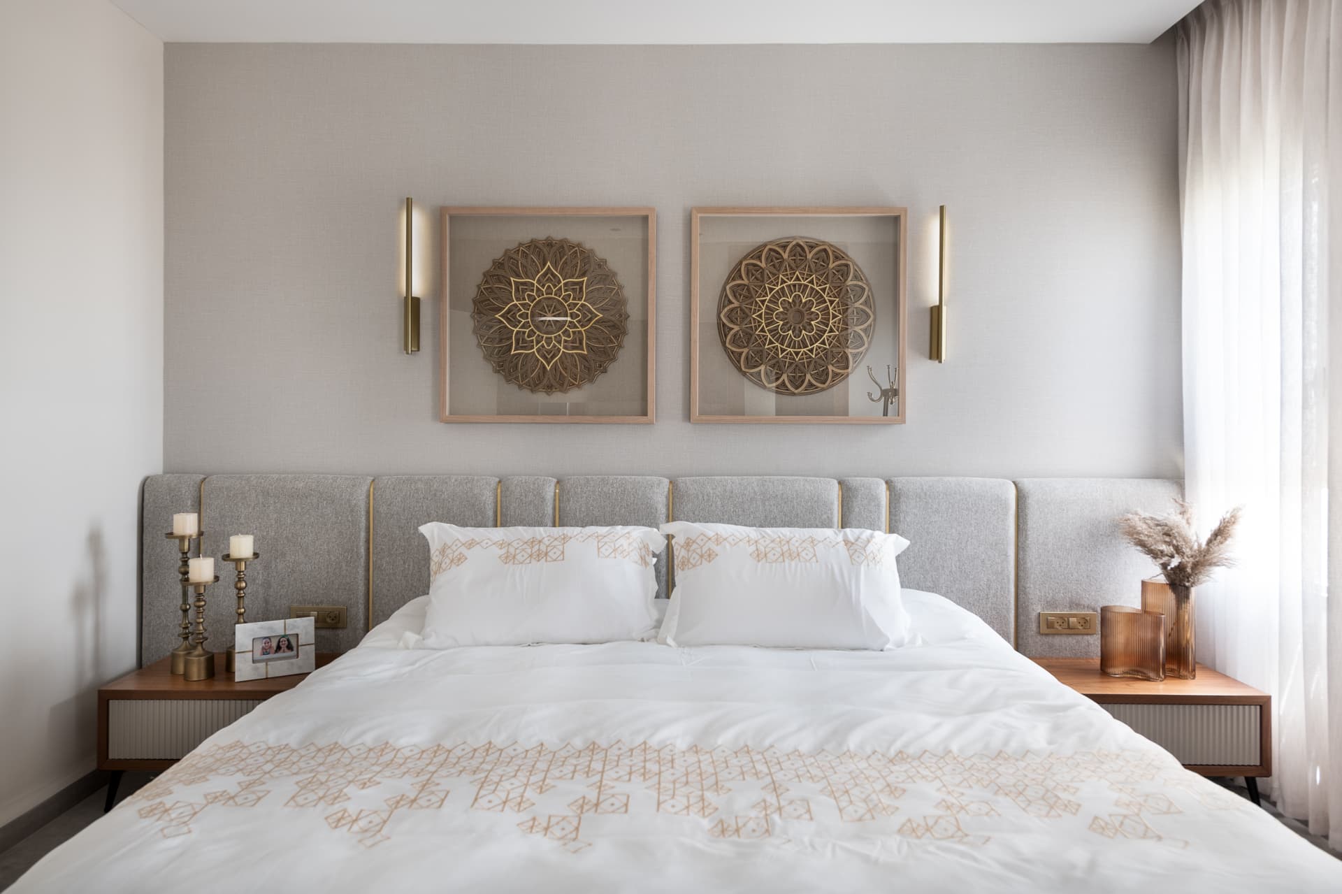 Grey panelled headboard with slim brass sconces flanking two framed mandala artworks above the bed in the master bedroom of Pistachio