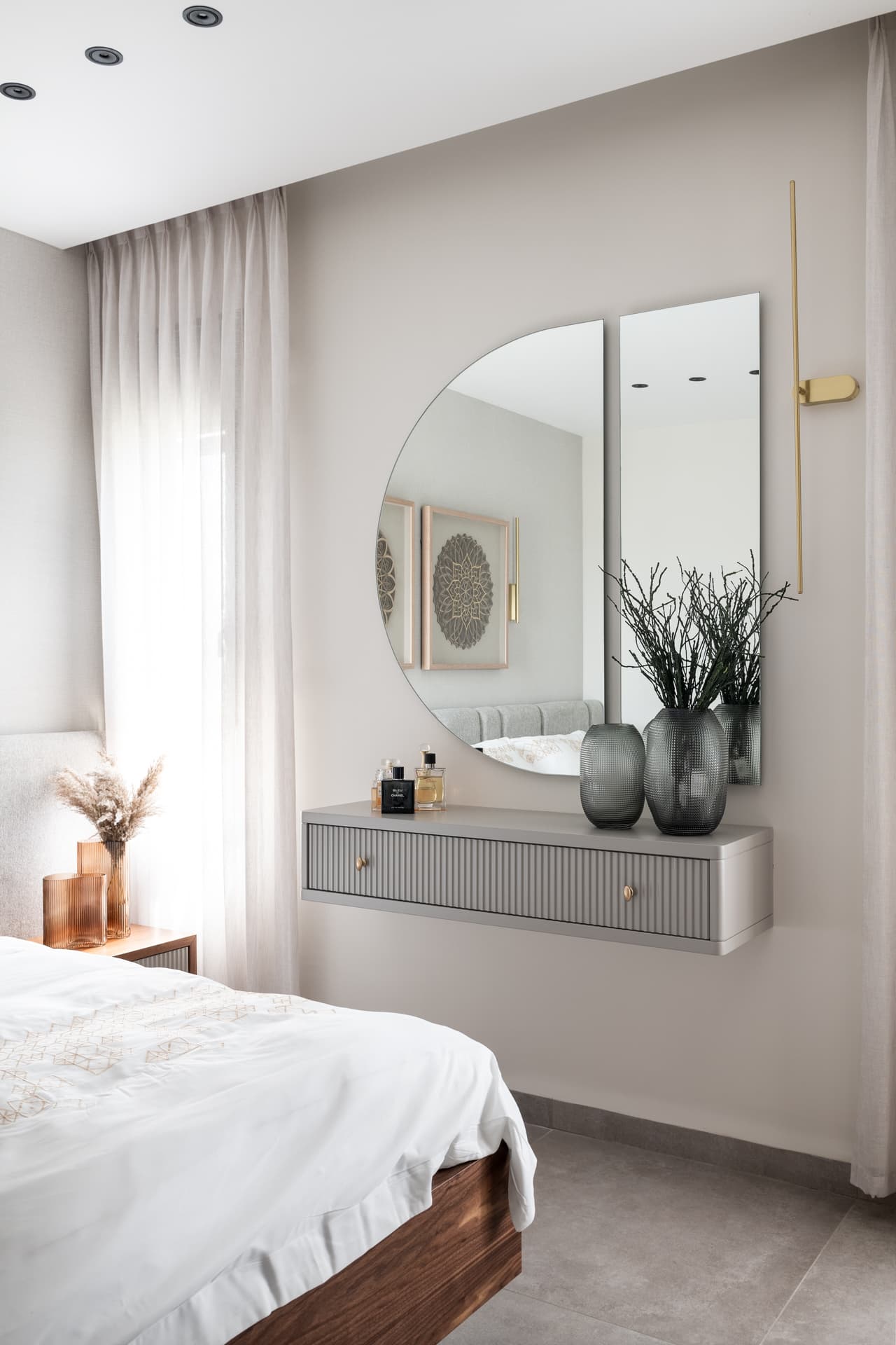 Floating fluted grey dressing console under a split round mirror with a slim brass wall light in the master bedroom of Pistachio
