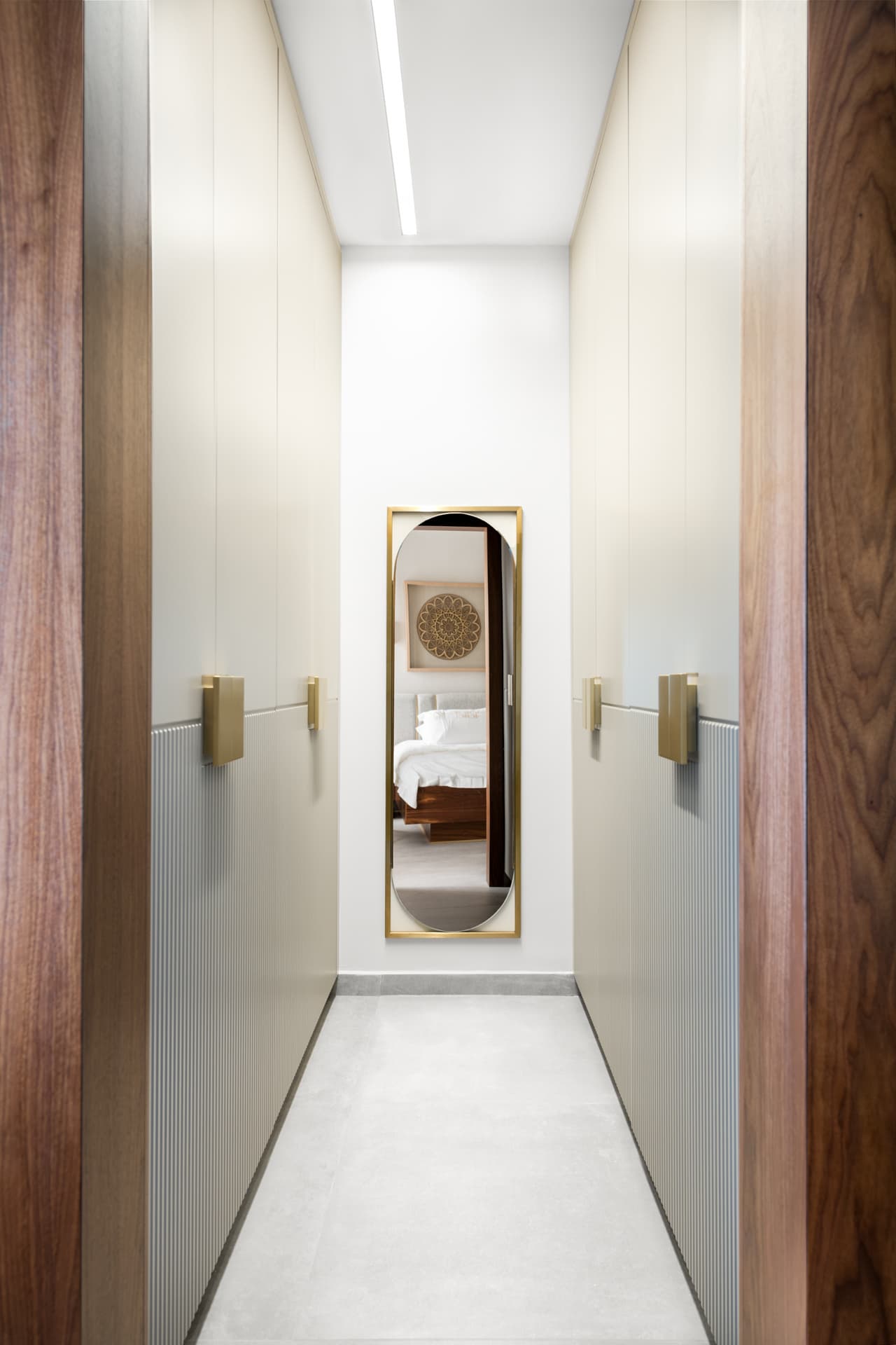 Narrow walk-in closet lined with fluted cream doors and brass handles, ending in a tall rounded brass-framed mirror in Pistachio