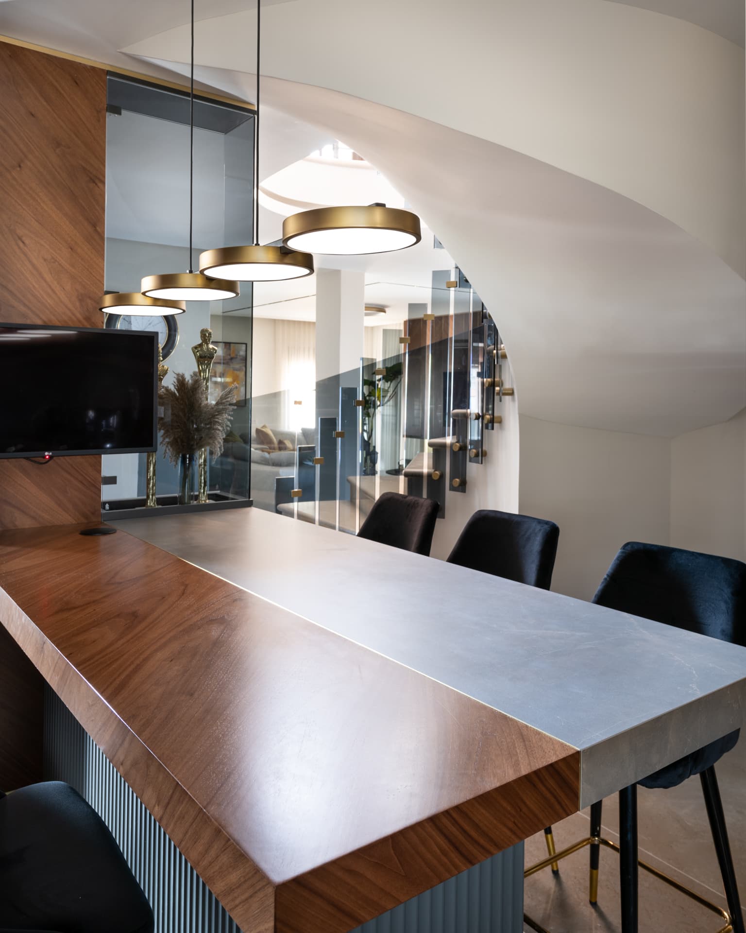 Walnut and grey stone bar counter under brass disc pendants, with a curved white staircase beyond, in the bar of Saffron