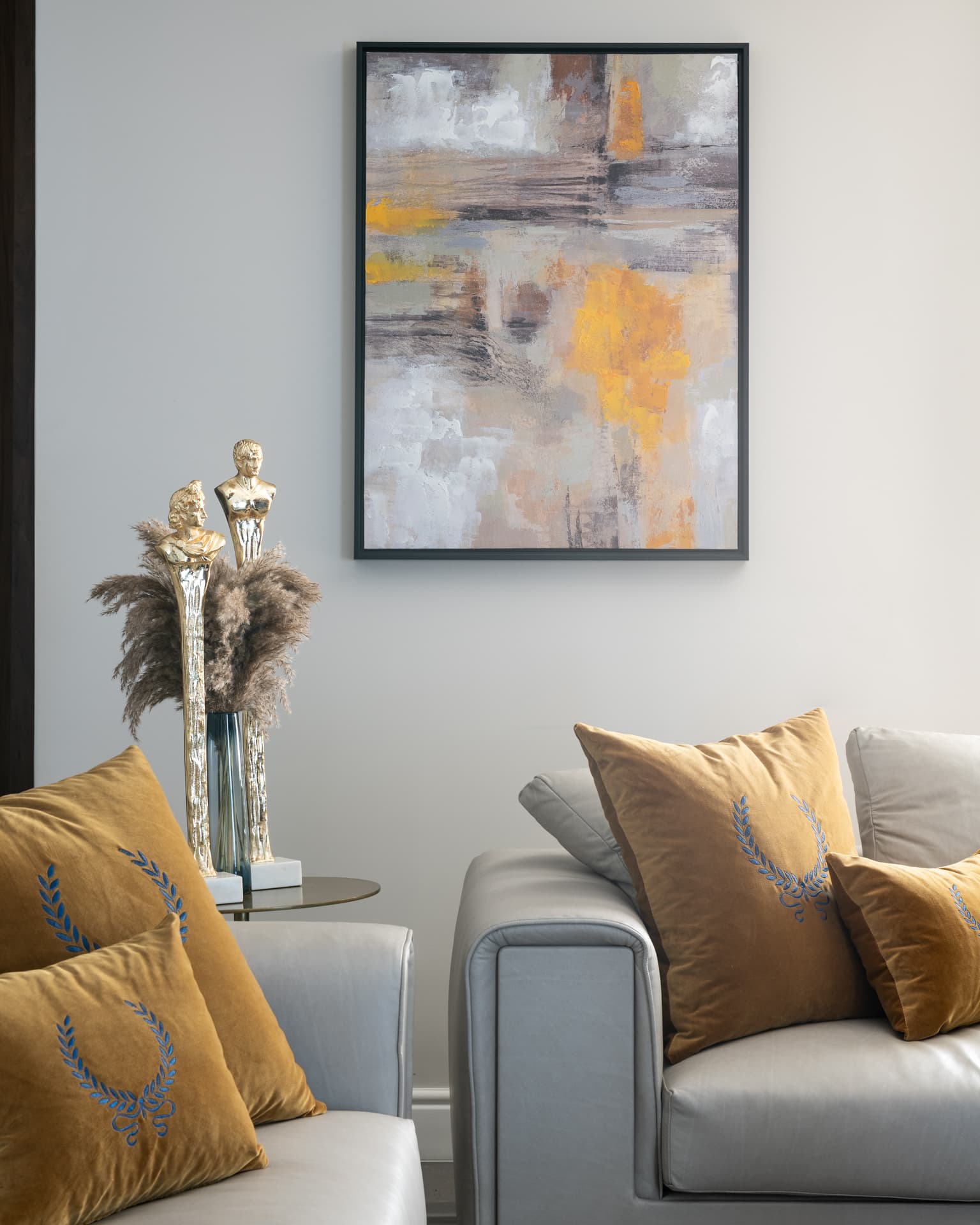 Laurel-embroidered ochre velvet cushions on grey leather sofas beneath an abstract painting in the living room of Saffron