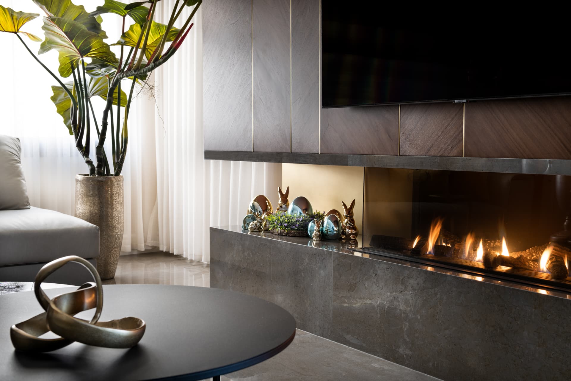 Sculptural brass knot on a black coffee table before a stone-clad linear fireplace in the living room of Saffron