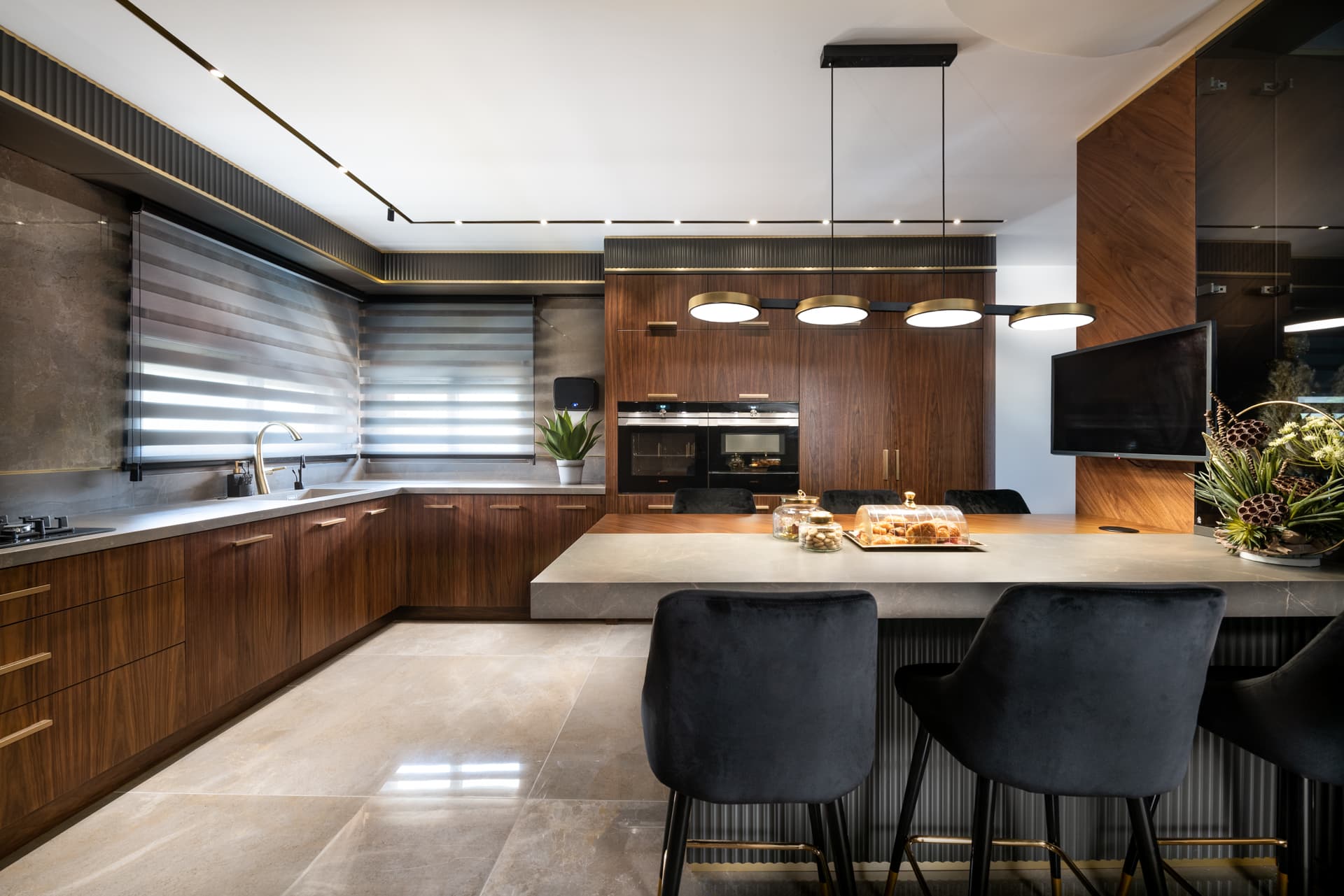 Walnut kitchen with a grey stone island, black velvet bar stools and a row of brass disc pendants in Saffron