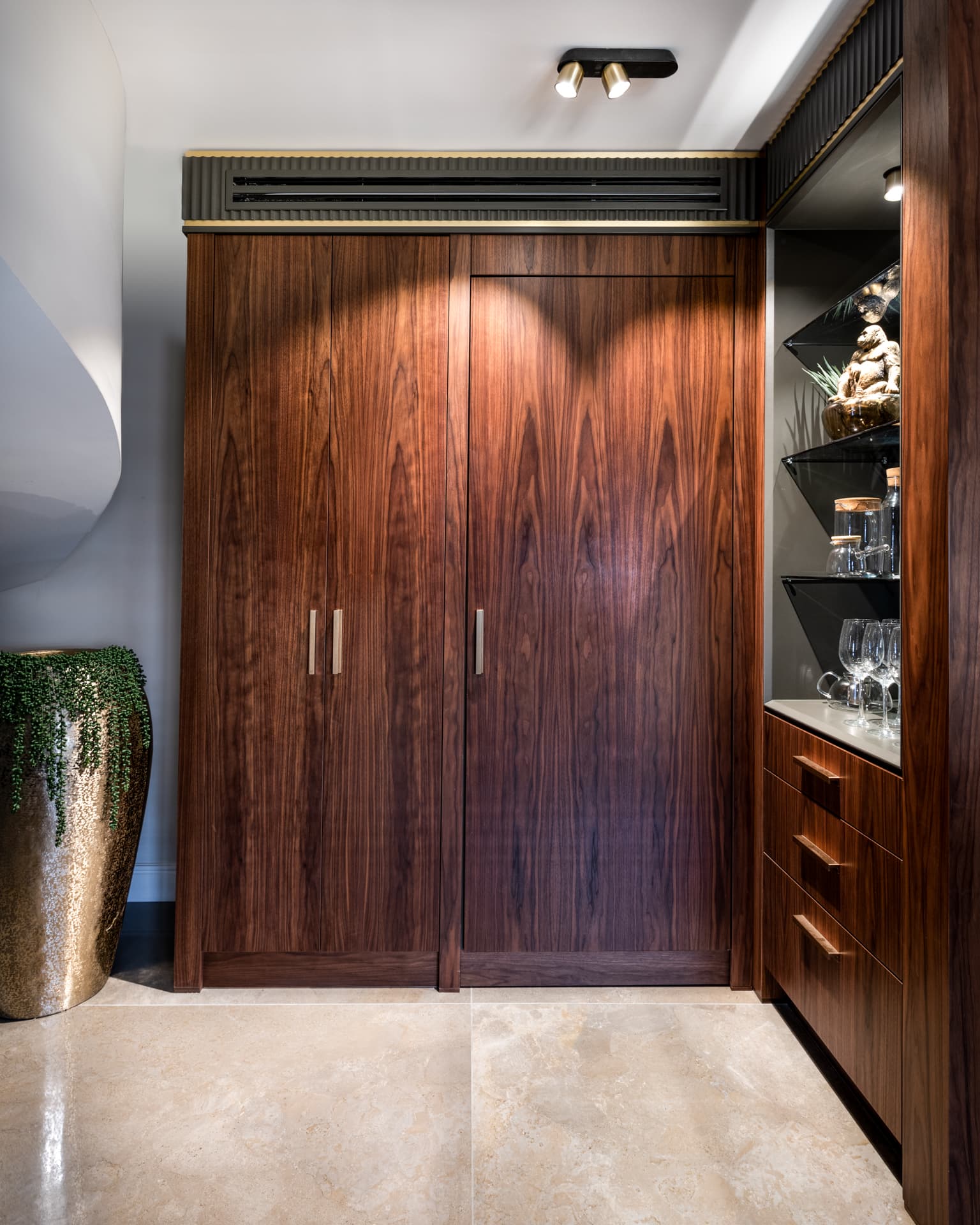Full-height walnut cabinet doors with slim brass pulls under a fluted black cornice in the kitchen of Saffron