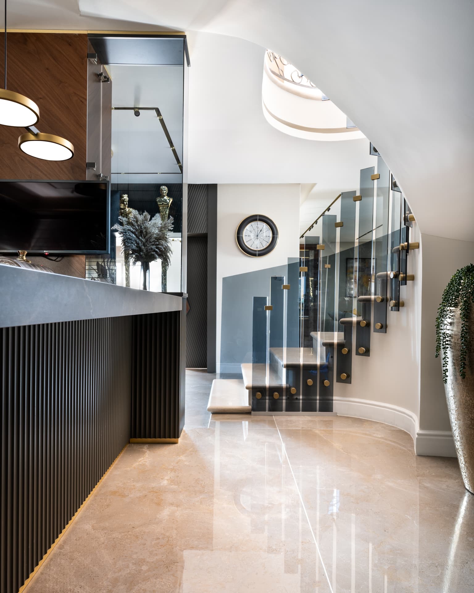 Floating stone treads with smoked-glass panels and brass fixings curving up a white stairwell, seen from the bar in Saffron