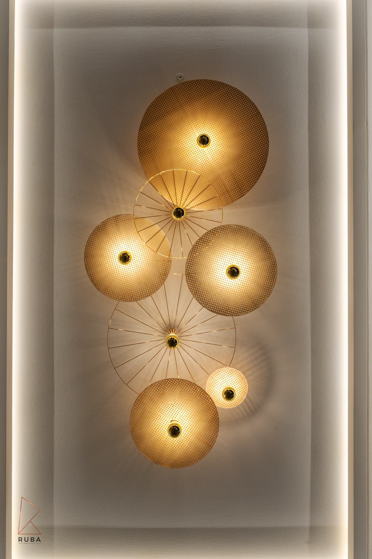 Wall light of overlapping gold mesh discs glowing inside a backlit recessed niche in The Last Supper