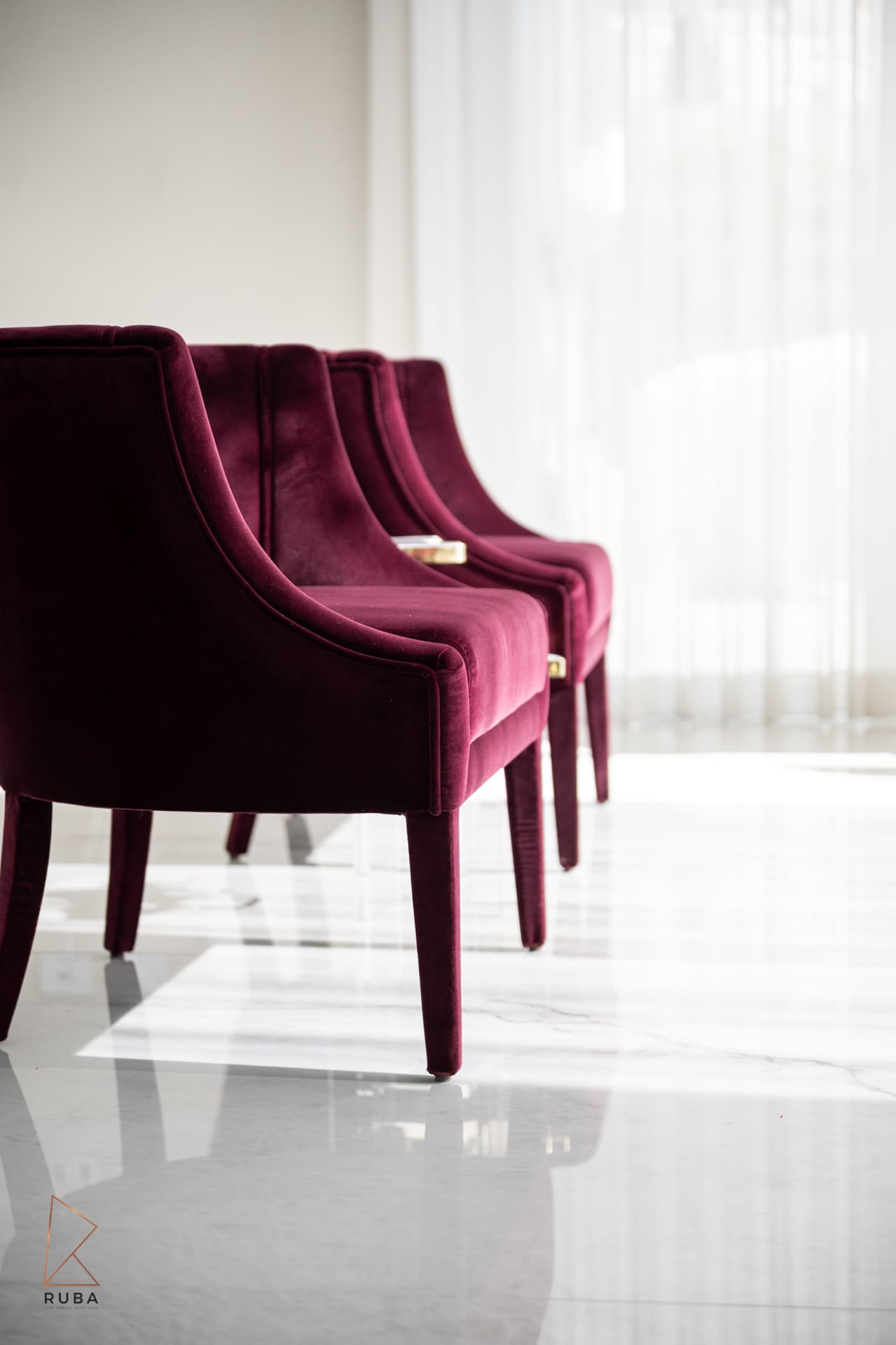 Row of burgundy velvet chairs with slim tapered legs on a glossy white floor in The Last Supper