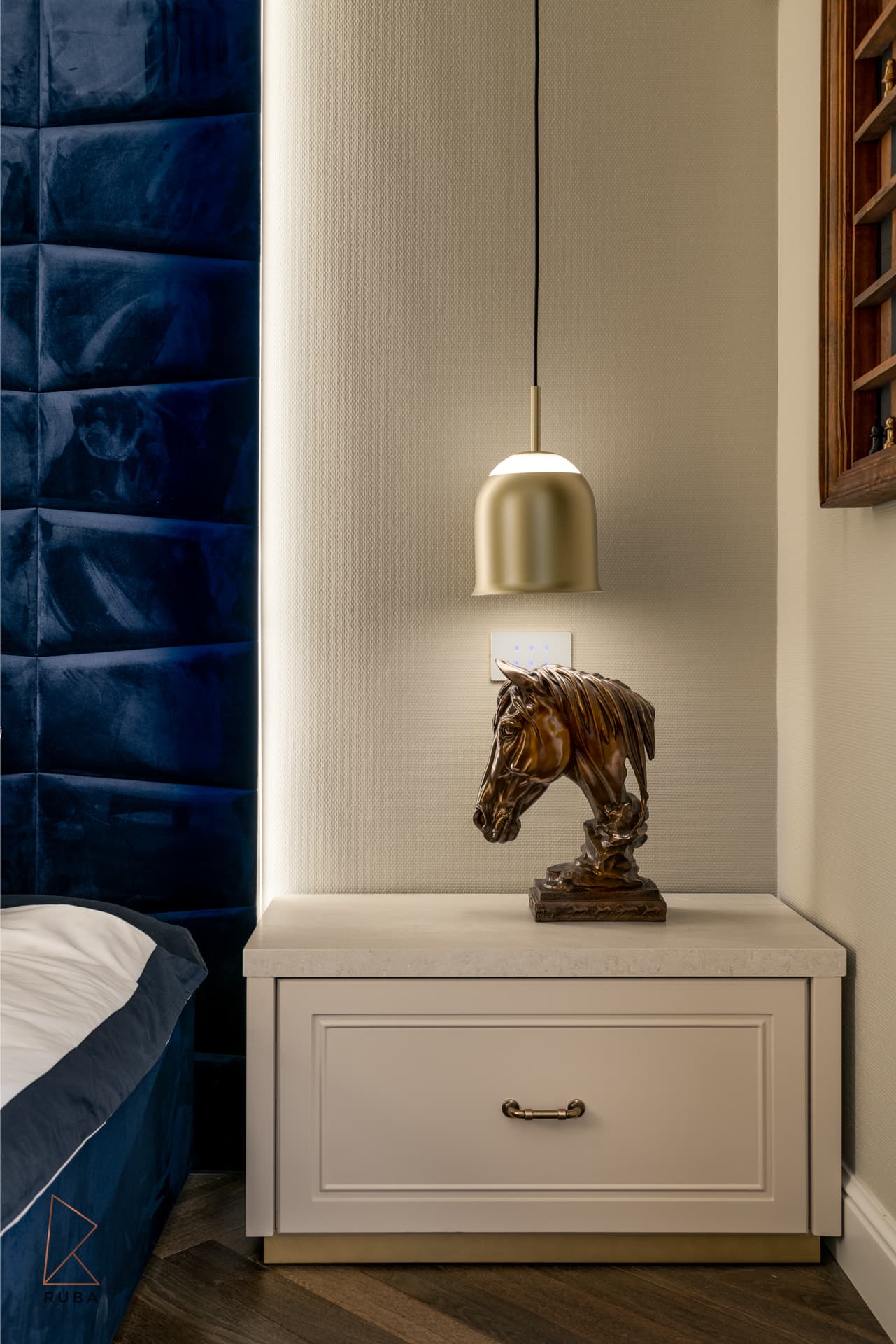 Cream nightstand with a brass bell pendant and carved horse bust beside a navy velvet headboard in The Last Supper