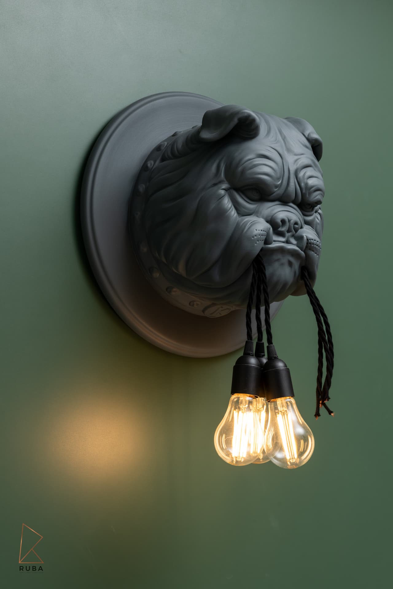 Close-up of a bulldog-head wall sconce with three filament bulbs on twisted cords against green paint in The Last Supper