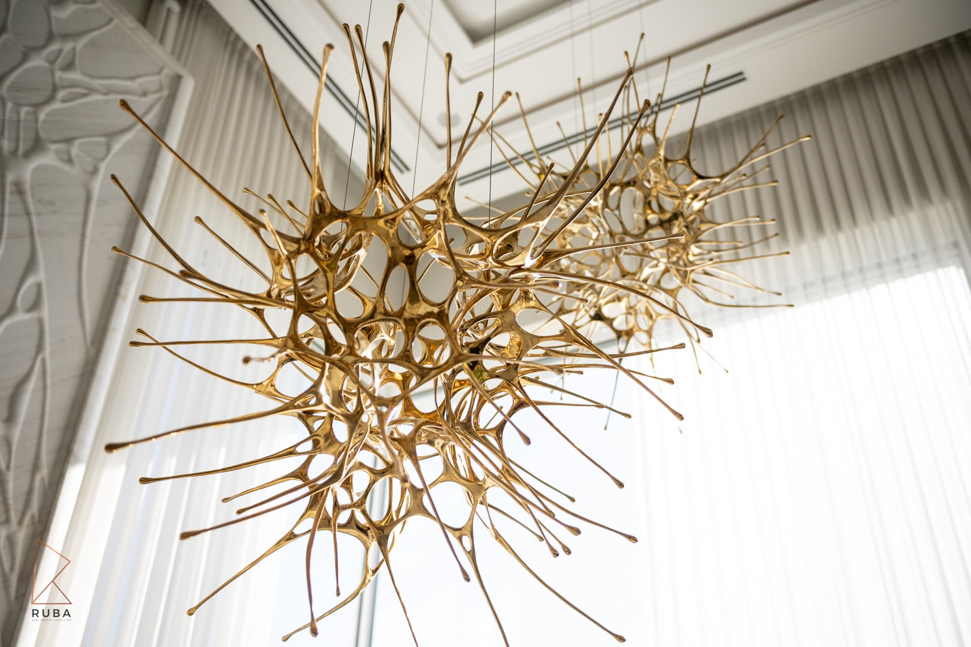 Looking up at a gold starburst chandelier with branching arms against sheer curtains in The Last Supper