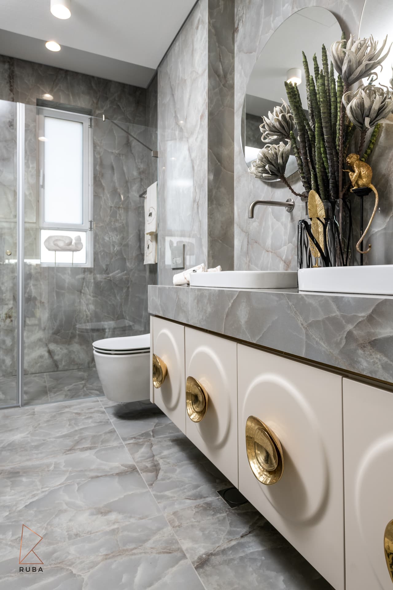 Kids bathroom with grey veined stone walls, floating carved vanity and wall-hung toilet beside the shower in The Last Supper