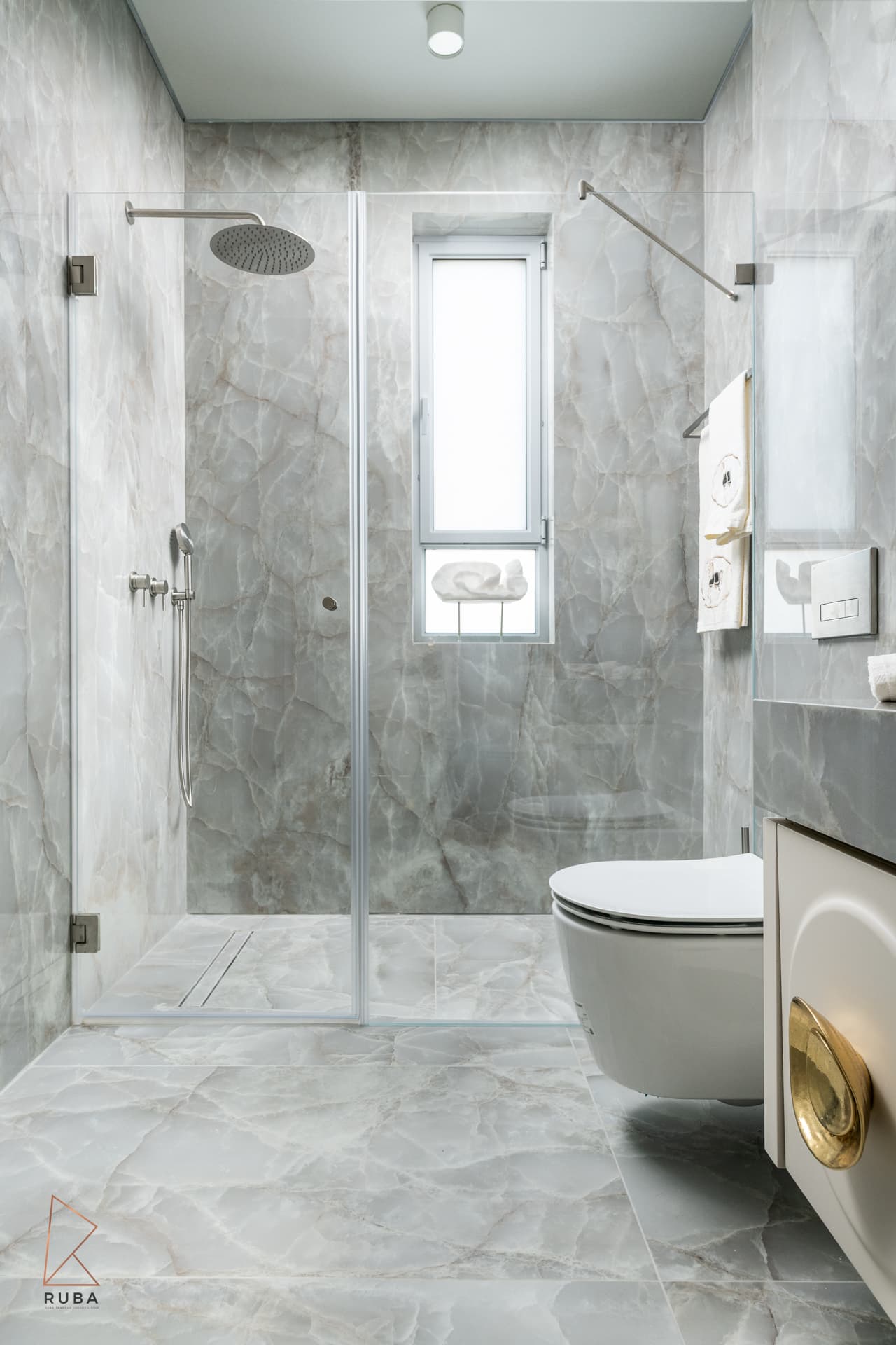 Walk-in glass shower lined in grey veined stone with a brushed rain head and linear drain in The Last Supper