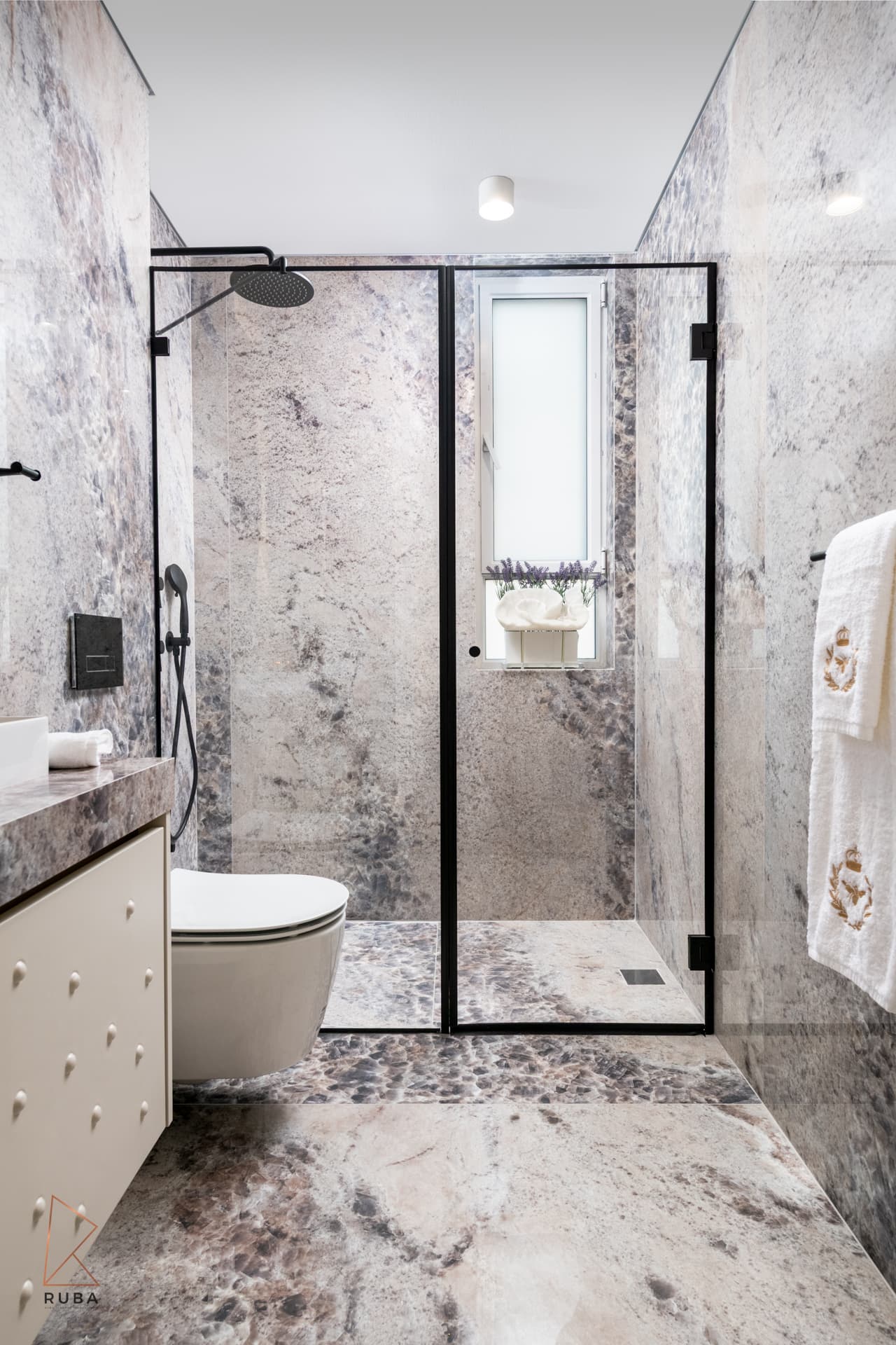 Bathroom with speckled grey-pink stone walls, black-framed glass shower and studded cream vanity in The Last Supper