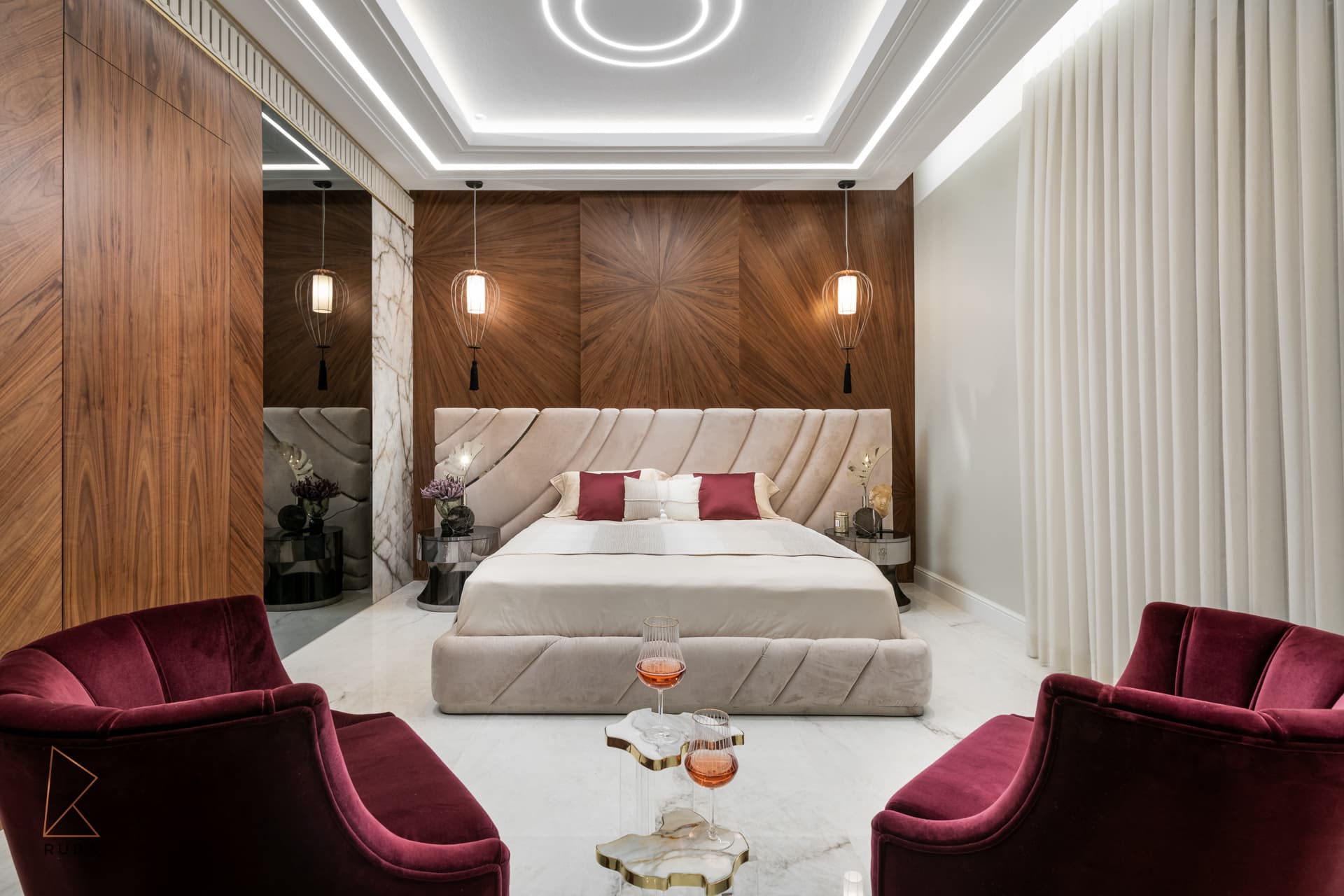 Master bedroom seen past two burgundy velvet armchairs and stone-topped side tables toward the walnut bed wall in The Last Supper