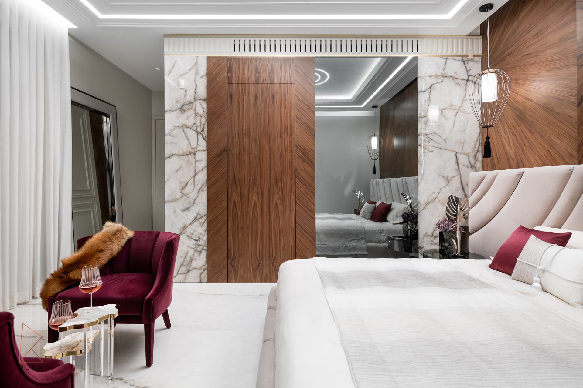 Master bedroom corner with a walnut door panel set in veined marble, a mirrored wall and a burgundy velvet armchair in The Last Supper