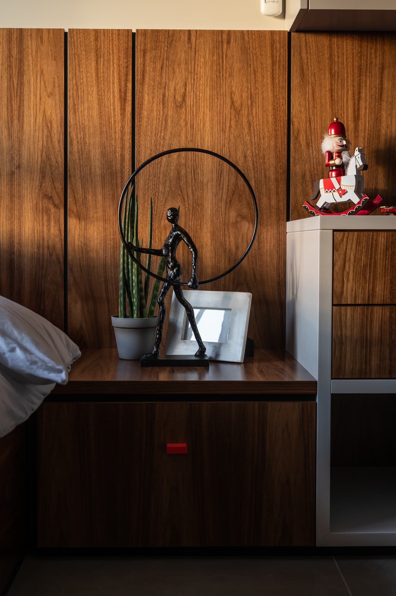 Walnut bedside unit with a hoop figure sculpture and small frame against vertical walnut panels in the boys room of Timeless Union