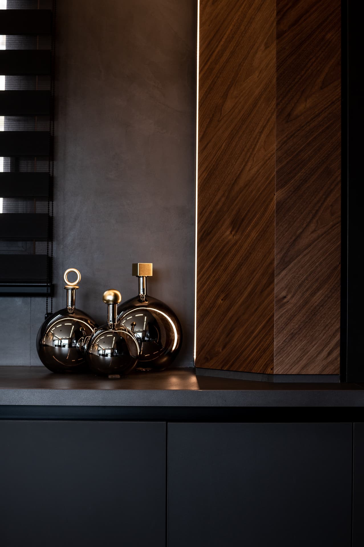 Trio of mirrored chrome decanters with brass stoppers on a dark counter beside walnut cladding in Timeless Union