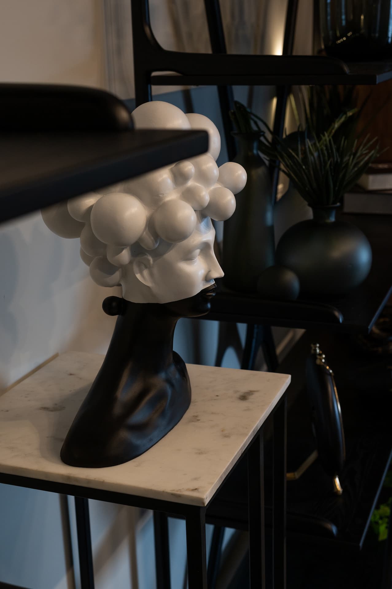 White bubble-curl bust with a black base on a veined marble side table beside black shelving in Timeless Union