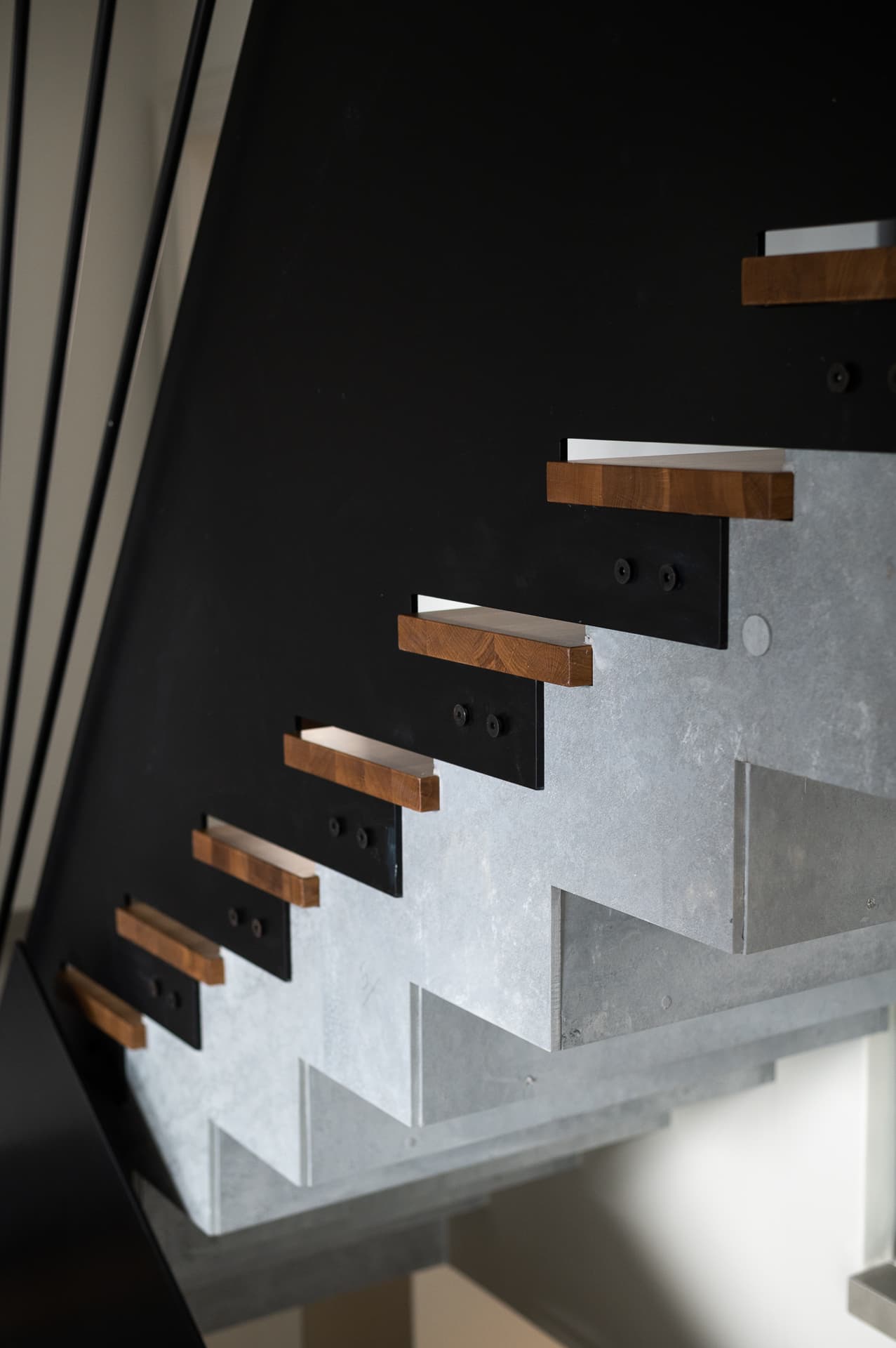 Oak tread ends bolted to a black steel stringer over a stepped grey concrete stair in Timeless Union