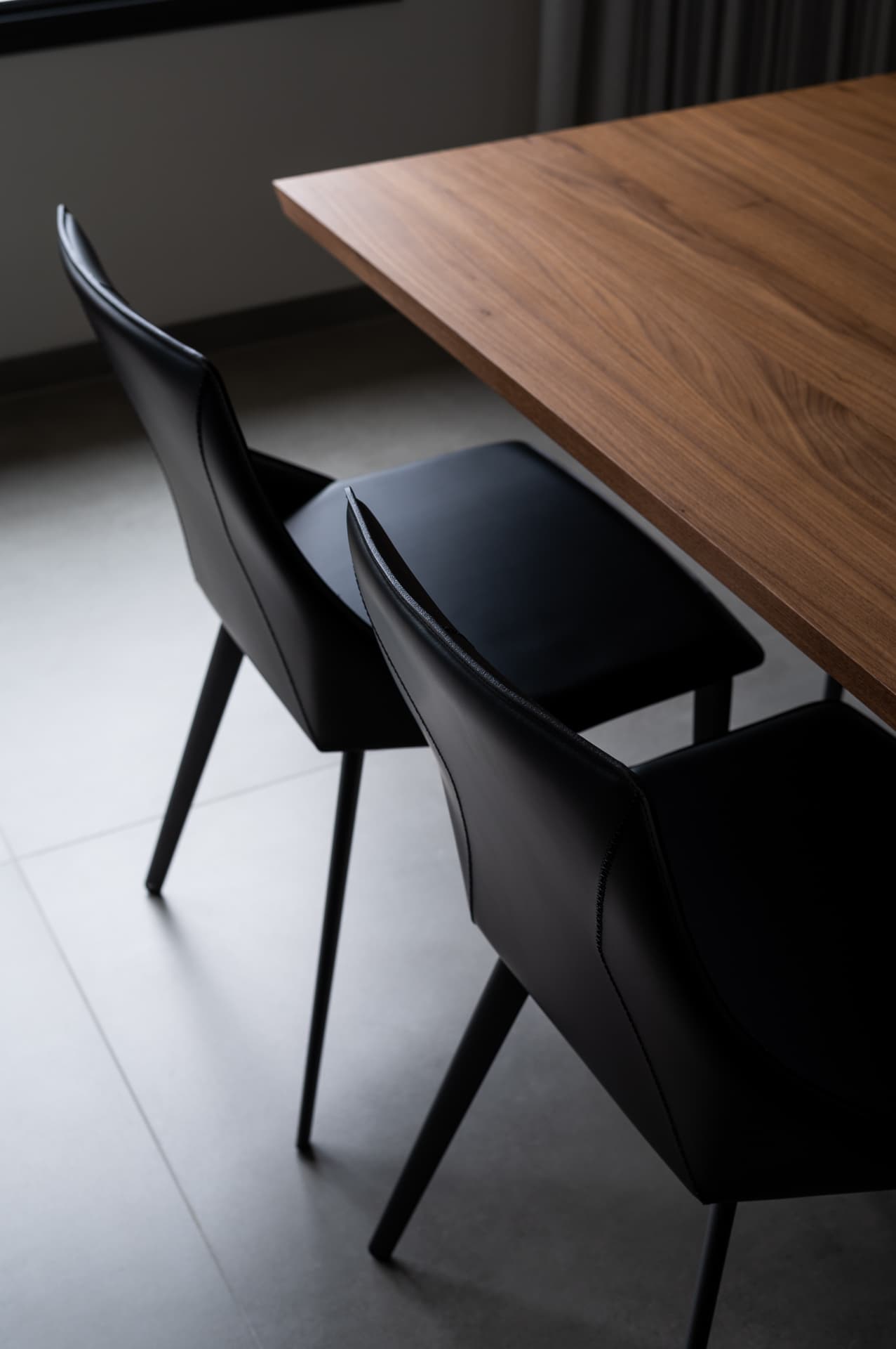 Black leather dining chairs tucked under a walnut table on pale stone-look tiles in Timeless Union