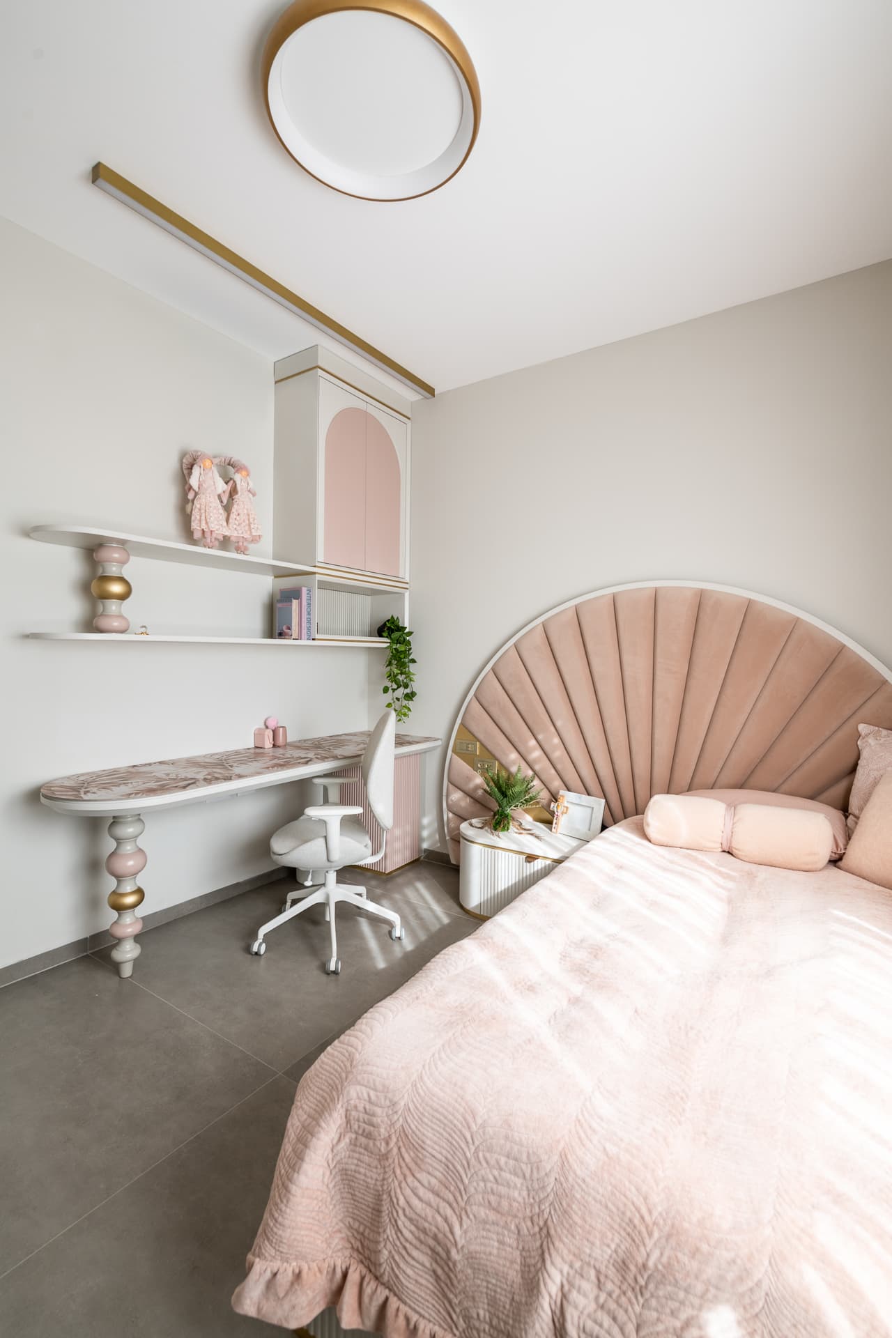 Girls room with a blush velvet fan headboard, gold-banded ceiling light and a desk on a turned pink and gold leg in Timeless Union
