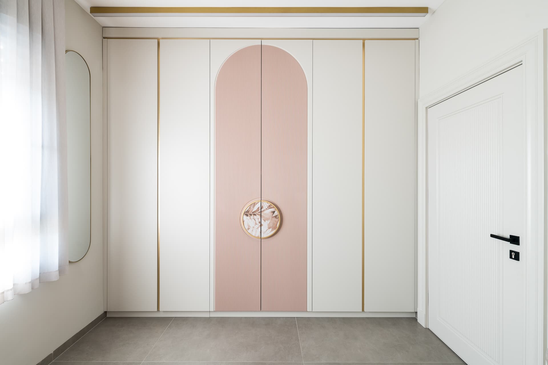 White wardrobe with an arched blush fluted centre, brass trim and a round botanical handle in the girls room of Timeless Union