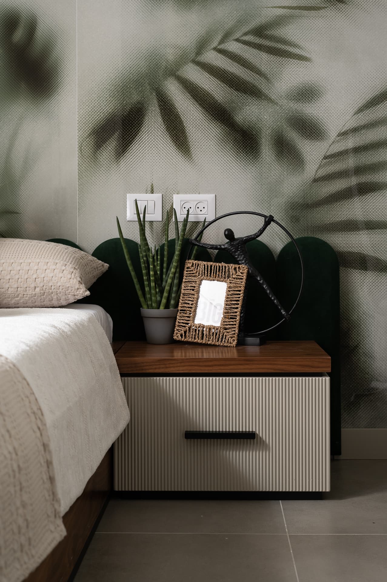 Fluted bedside drawer with a walnut top before arched green velvet panels and a leaf-print wall in the guest bedroom of Timeless Union