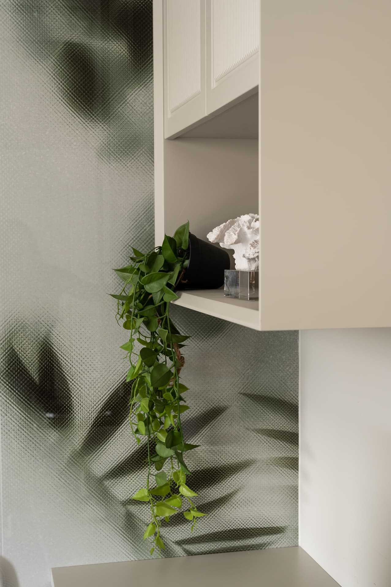 Trailing plant on an open shelf of a pale cabinet against a blurred leaf-print wall in the guest bedroom of Timeless Union