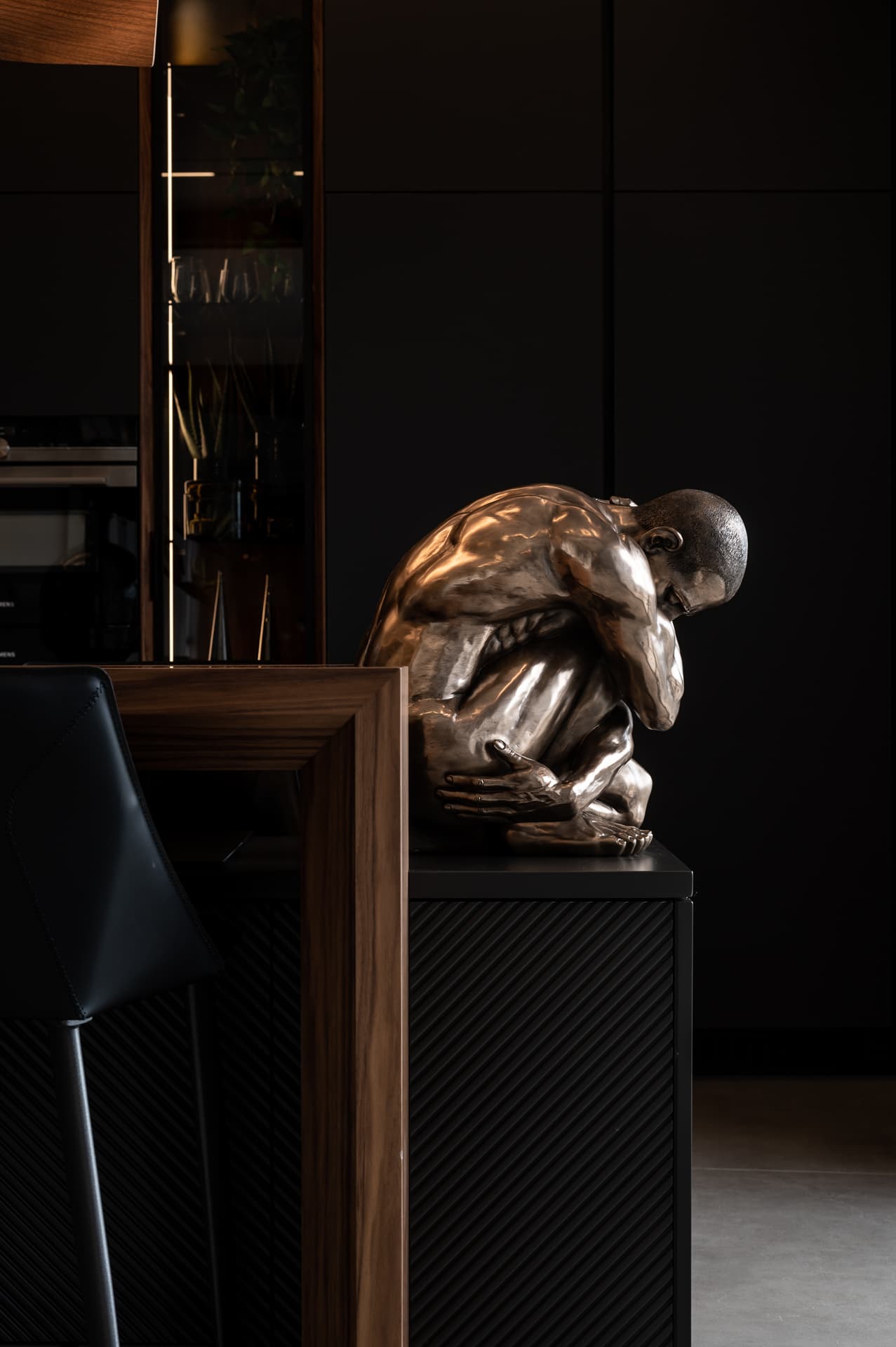Close-up of a crouching bronze figure sculpture on a ribbed black plinth against dark cabinetry in the kitchen of Timeless Union