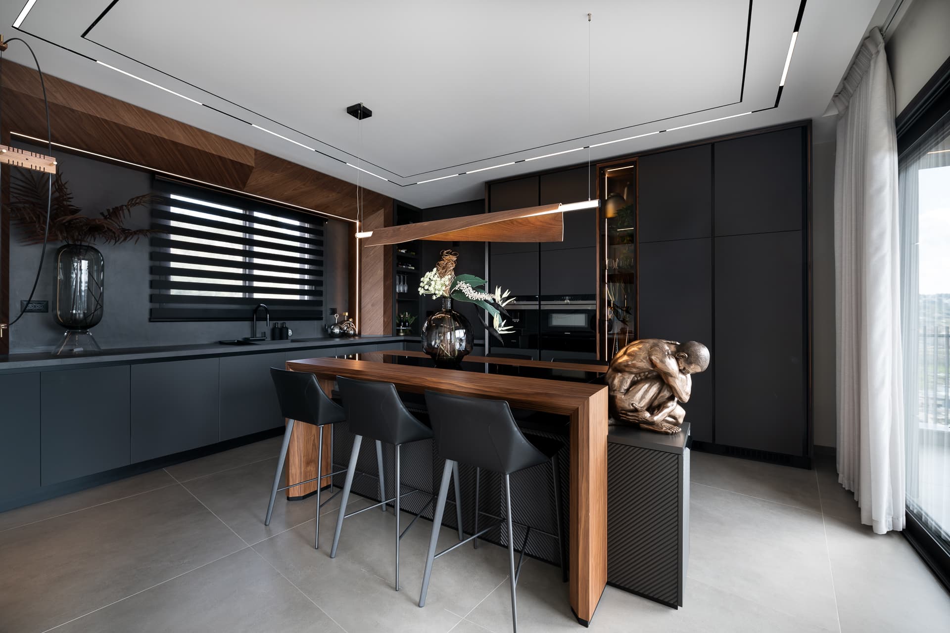 Dark kitchen with walnut-clad window niche, zebra blinds and a waterfall walnut island seen from the corner in Timeless Union