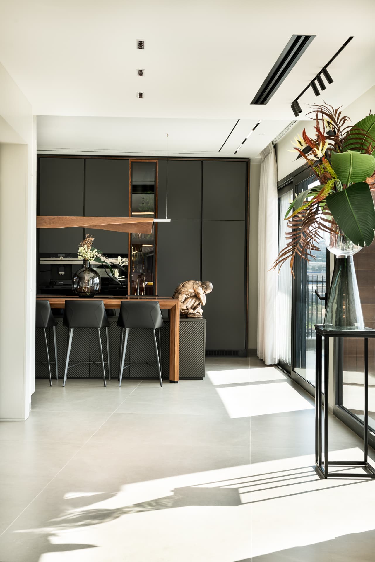 Kitchen island and tall graphite cabinetry seen past a tropical floral arrangement in the kitchen of Timeless Union