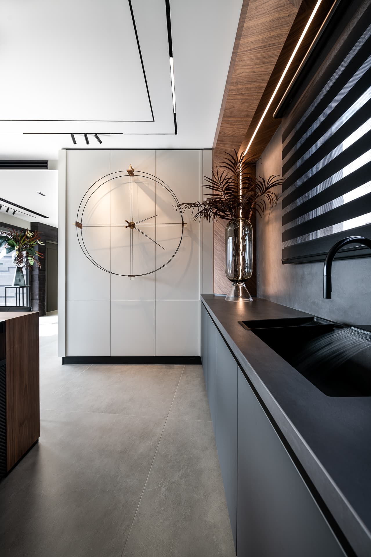 Oversized open wire clock on white panelled cabinetry beside a black sink counter in the kitchen of Timeless Union