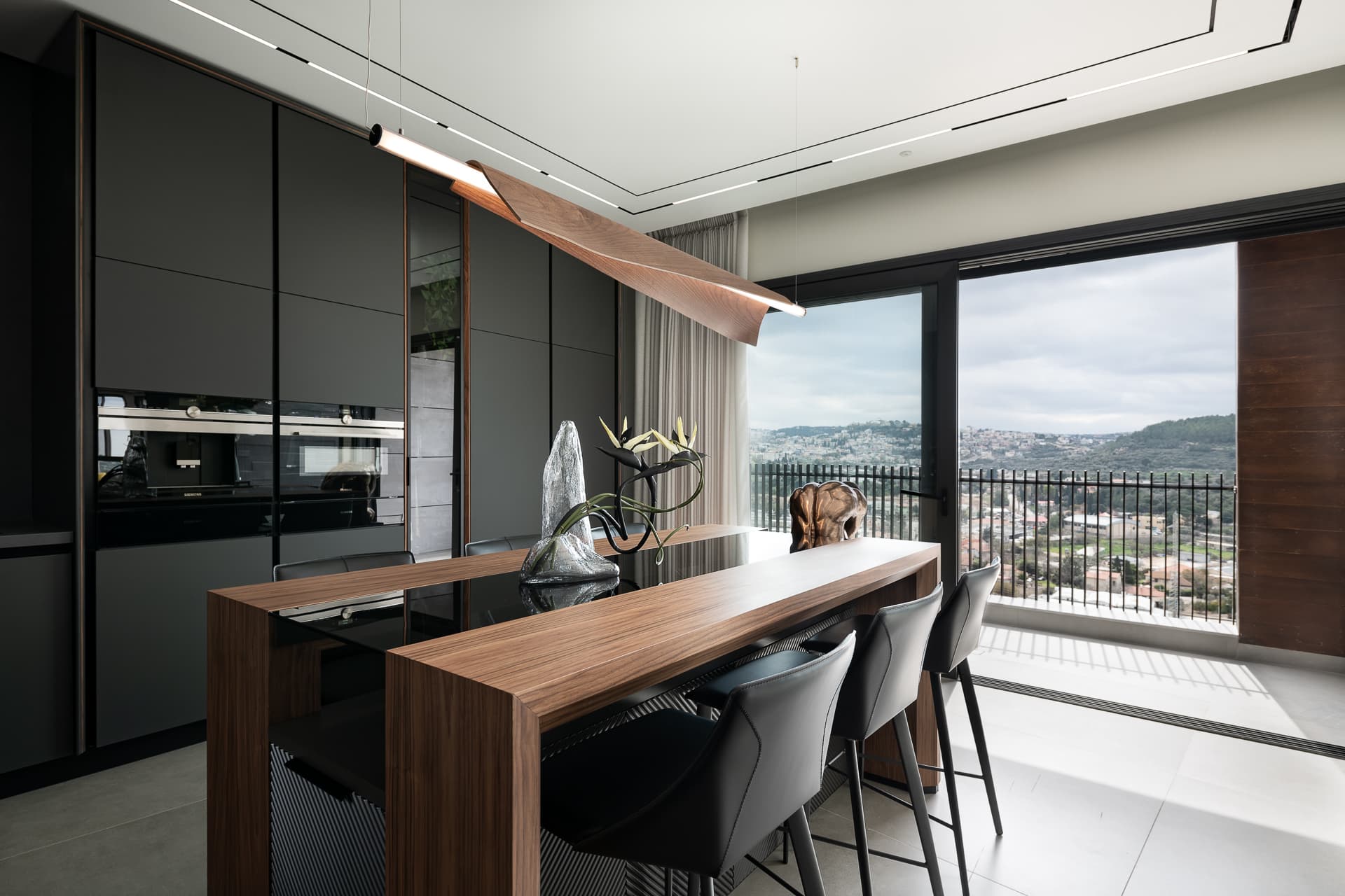 Walnut island with glass inset and black bar stools facing a wide glass door to the balcony in the kitchen of Timeless Union