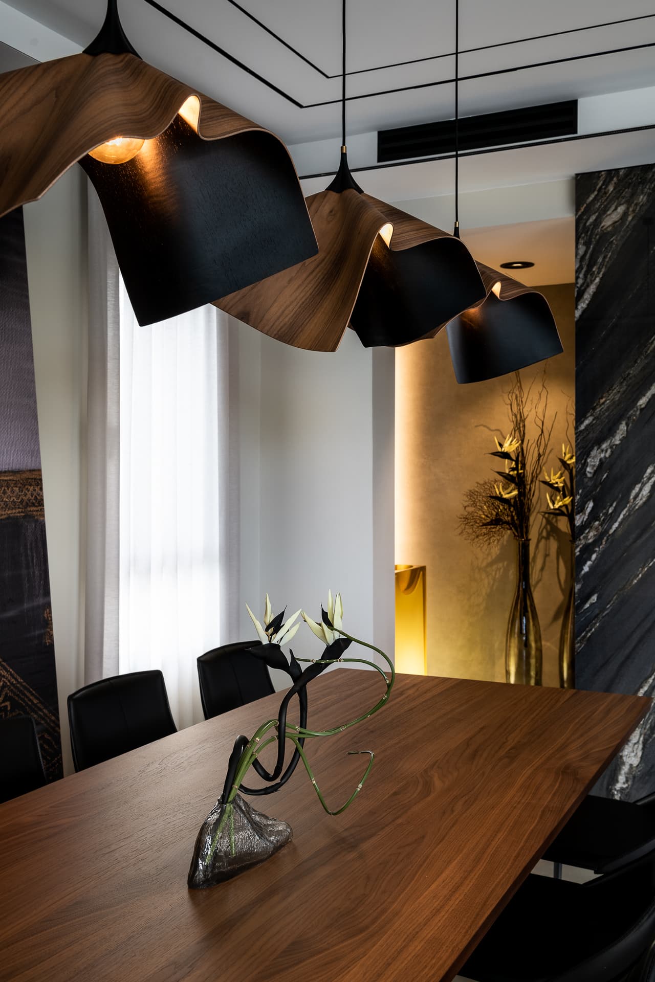 Wavy walnut and black pendant lamps over a walnut dining table with a sculptural vase in the dining area of Timeless Union