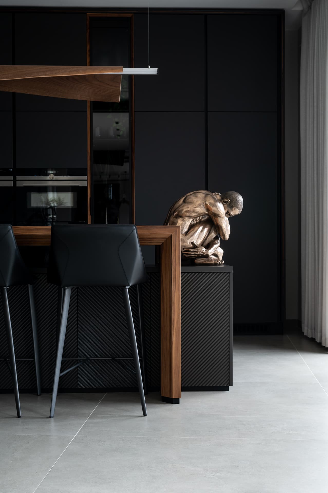 Crouching bronze figure sculpture at the end of the walnut island, with ribbed black base and stools, in the kitchen of Timeless Union