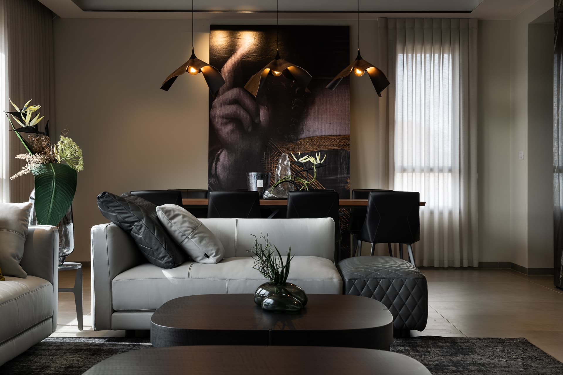 Grey leather sofa and quilted ottoman framing the dining table beneath three folded pendants in the living room of Timeless Union