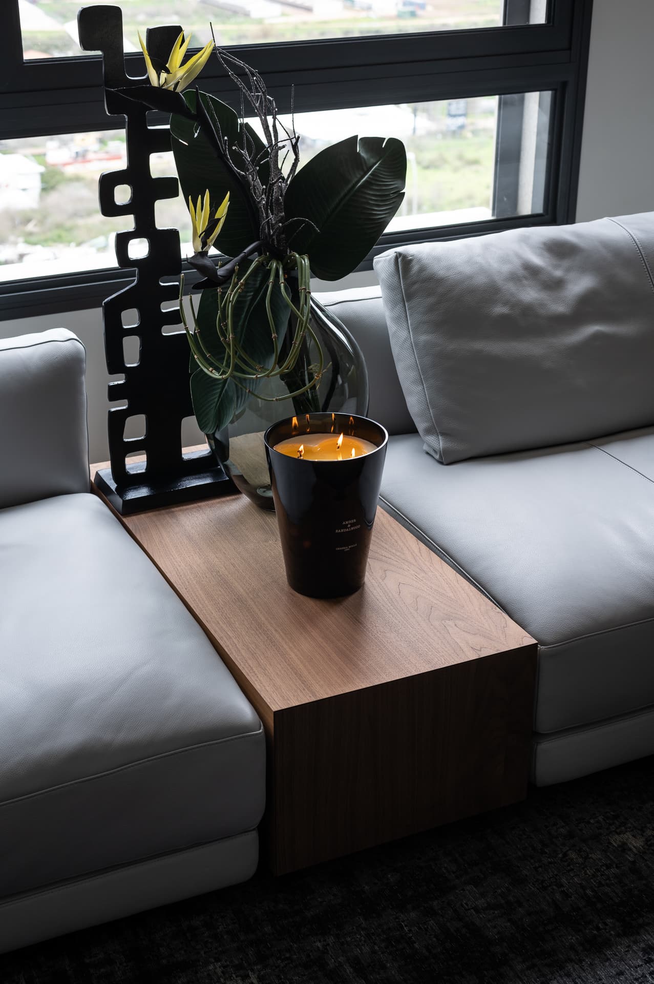 Walnut console bridging two grey leather sofa modules, holding a candle, glass vase and black sculpture in the living room of Timeless Union