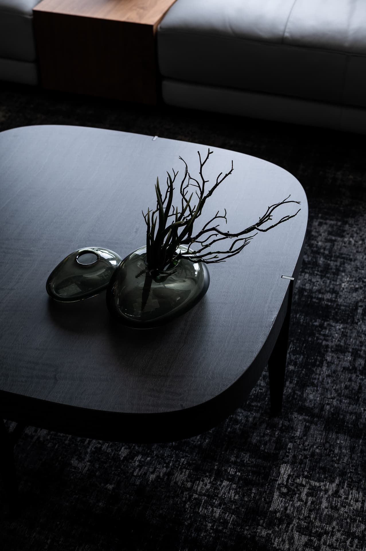 Smoked glass pebble vases with dark branches on a rounded black wood coffee table in the living room of Timeless Union