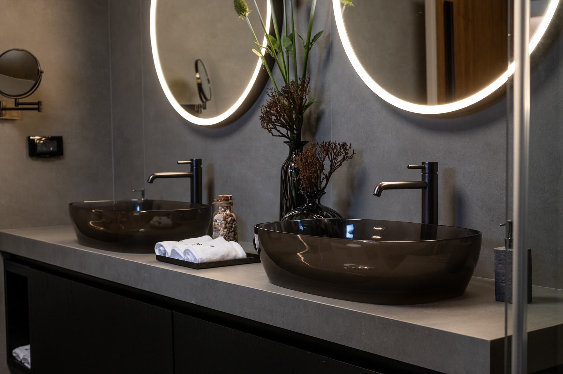 Double vanity with smoked glass vessel basins, black mixers and backlit round mirrors in the master bathroom of Timeless Union