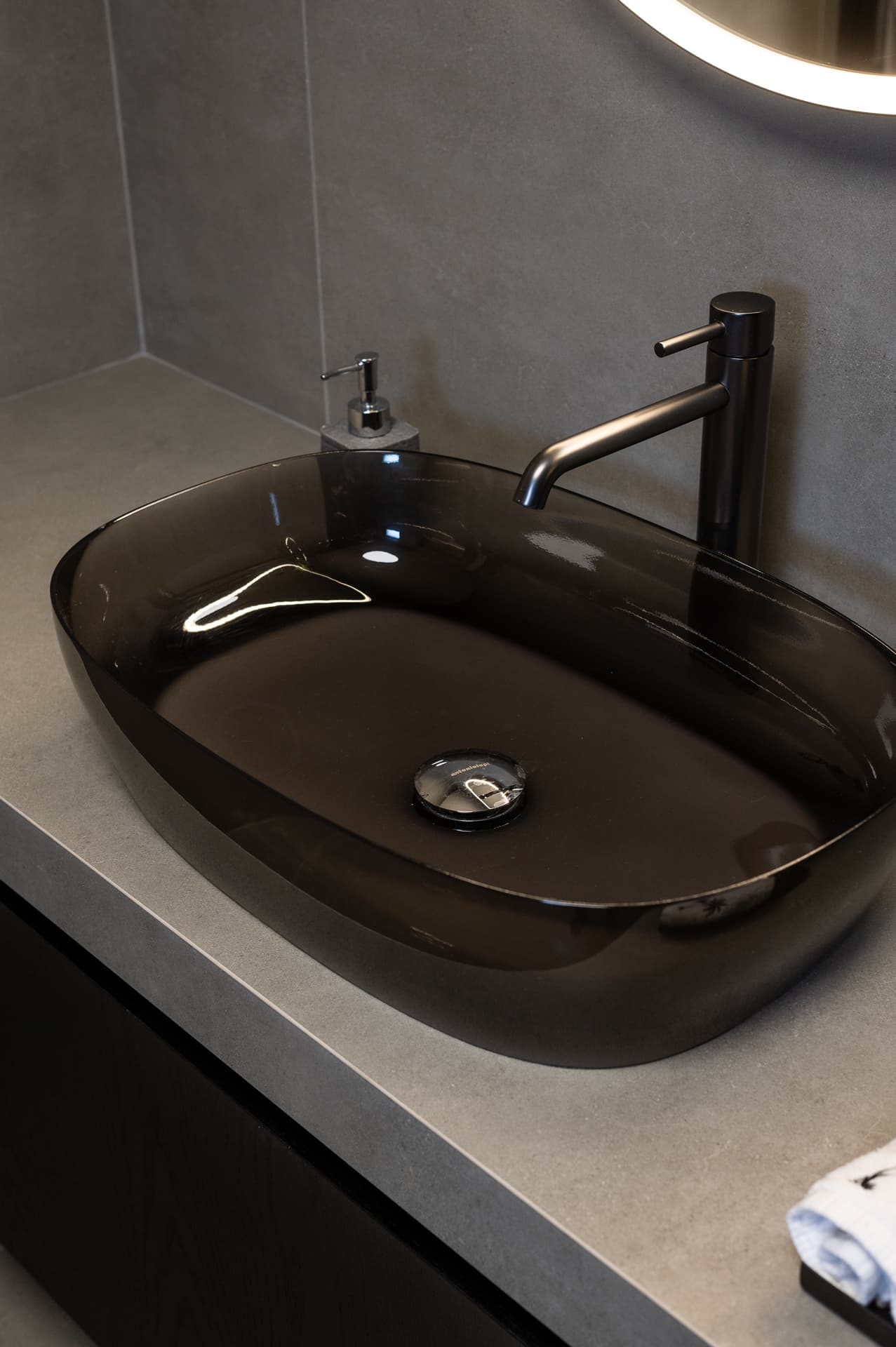Close-up of a smoked glass oval basin with a tall dark mixer on a grey stone counter in the master bathroom of Timeless Union
