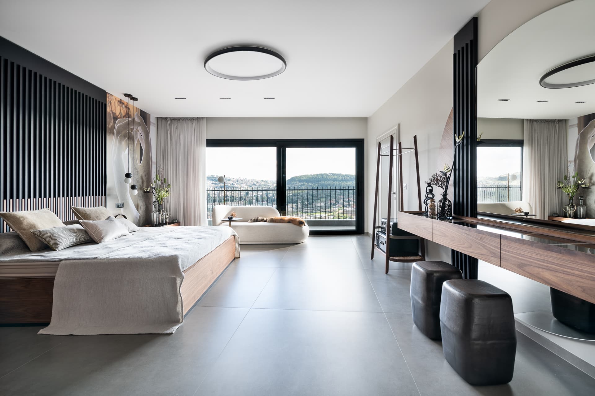 Open master bedroom with a black slatted wall, walnut platform bed and a floating walnut vanity with a round mirror in Timeless Union