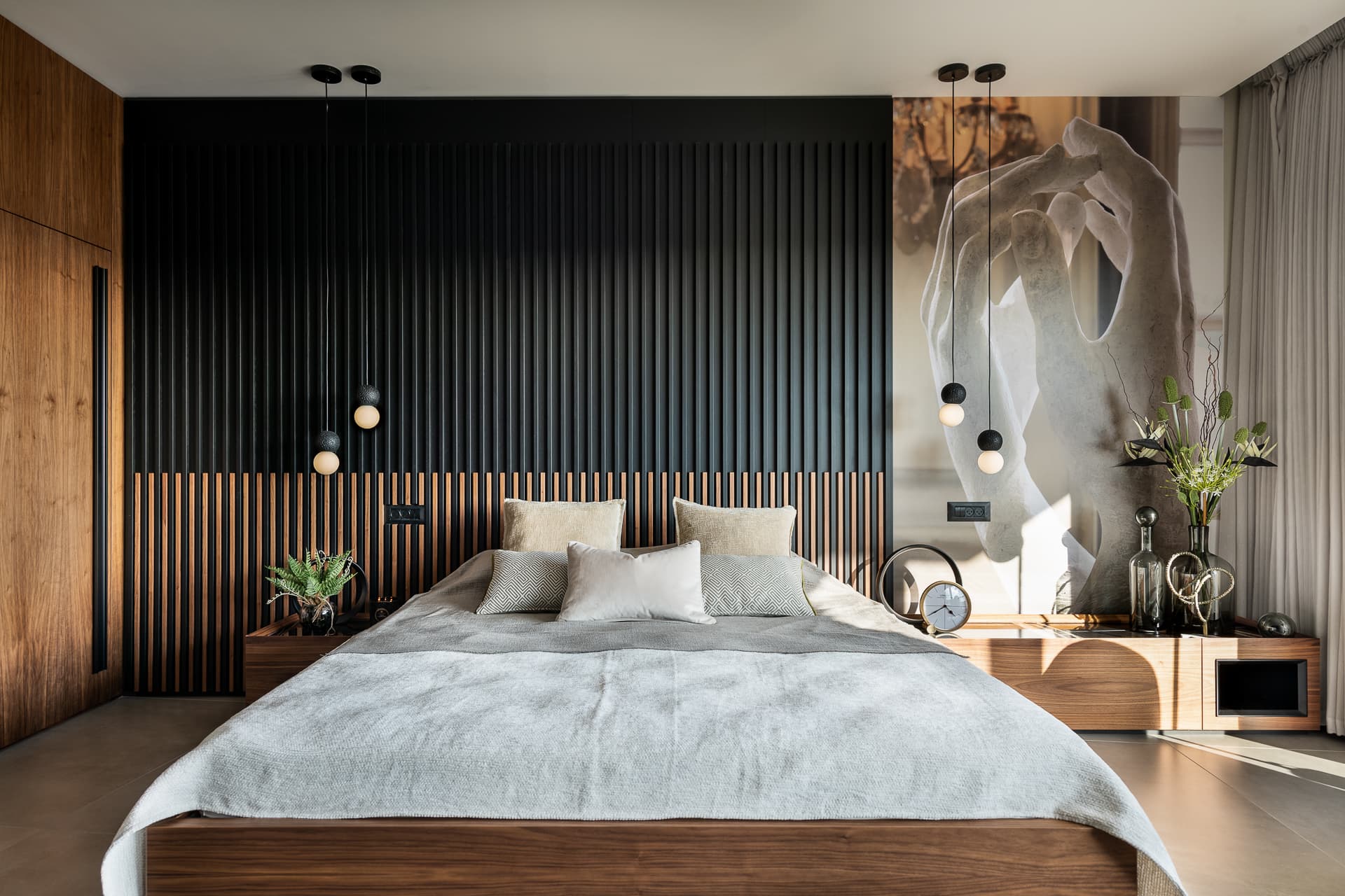 Walnut platform bed against a black slatted headboard wall with a large sculpted hands artwork in the master bedroom of Timeless Union
