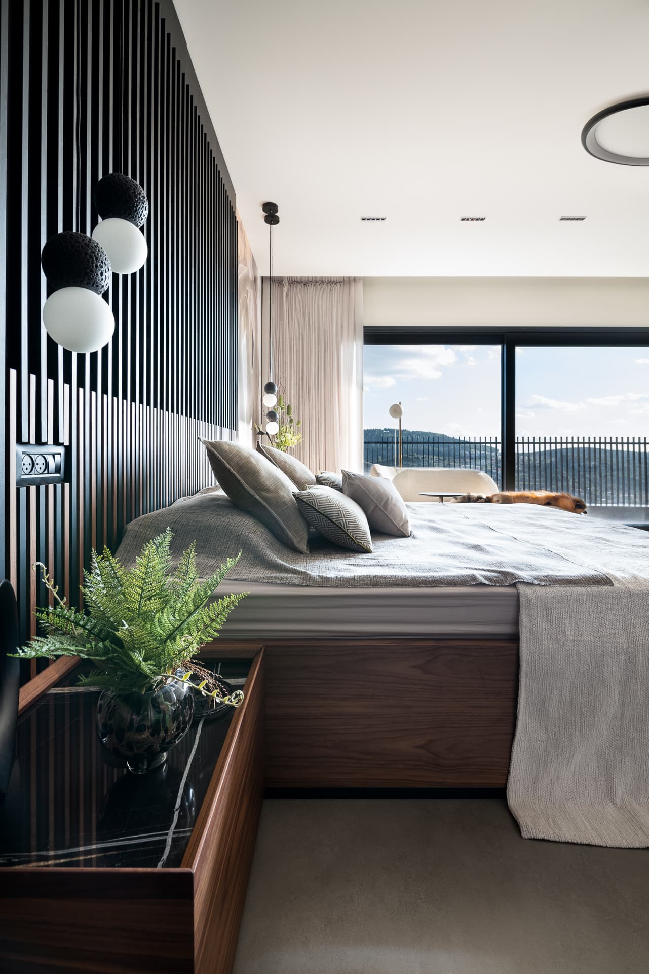 Textured orb pendants over a walnut and black stone nightstand, looking past the bed to the windows of the master bedroom of Timeless Union