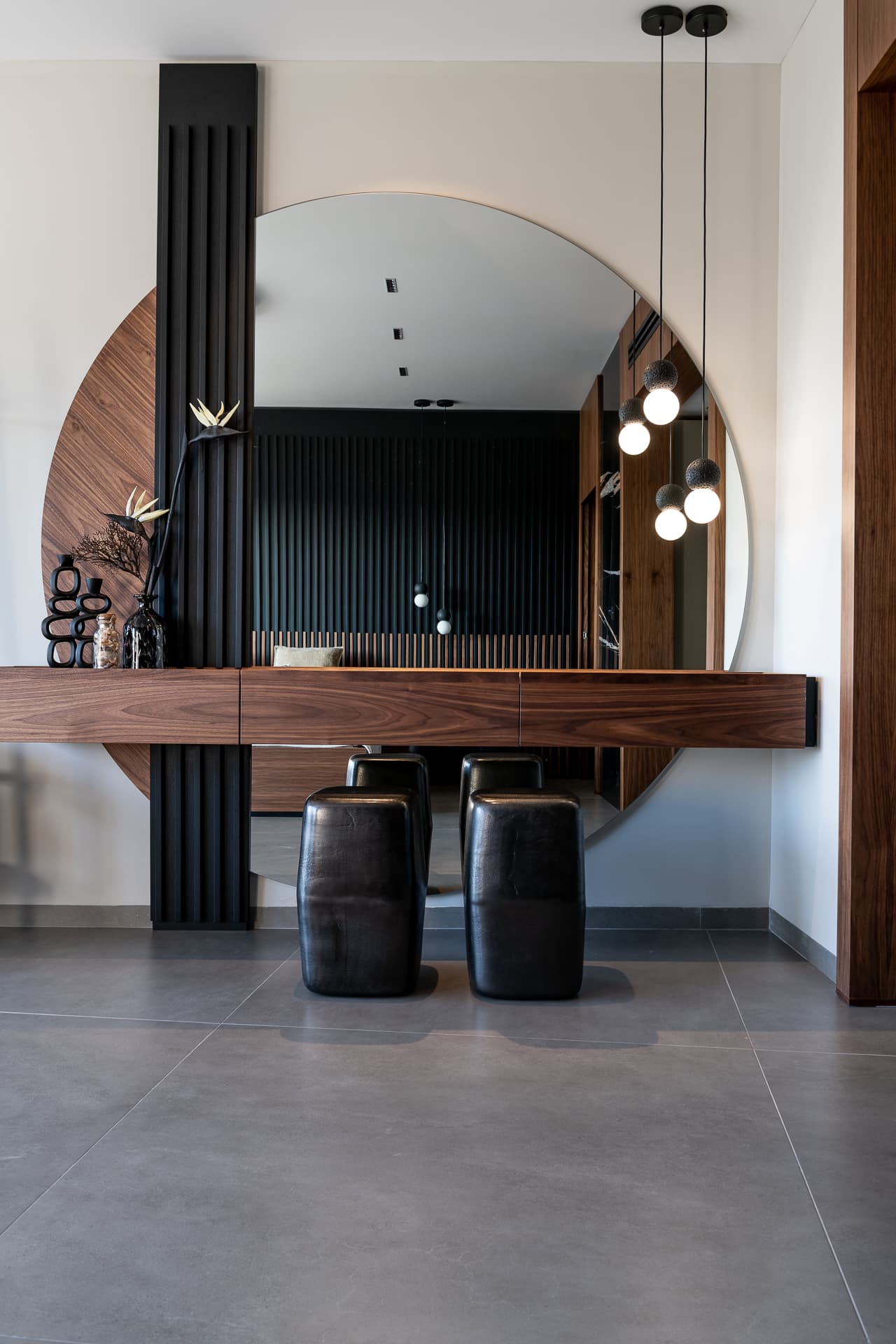 Floating walnut vanity split by a black fluted column against a large round mirror in the master bedroom of Timeless Union